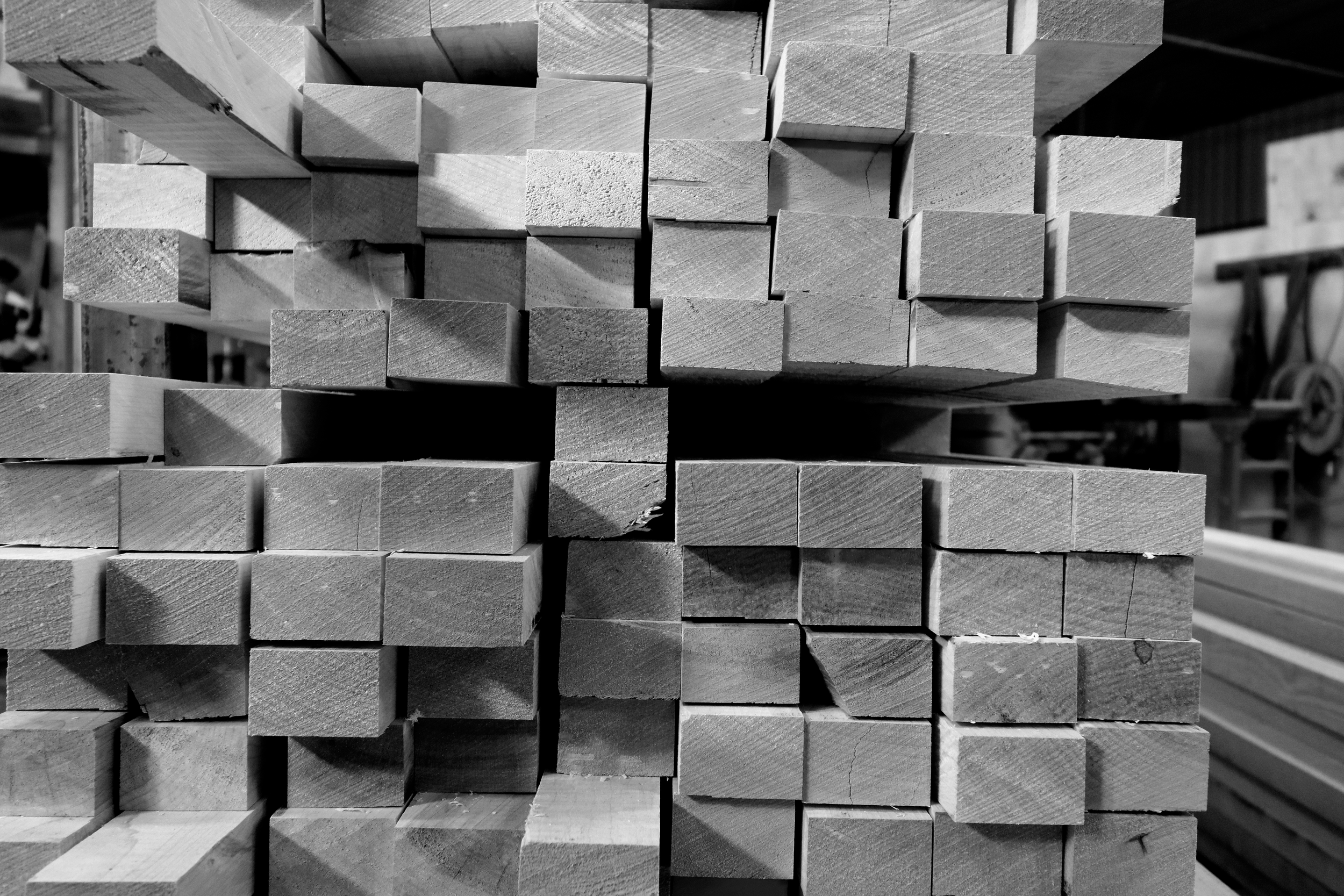 Stacks of wooden planks arranged in a workshop or lumberyard, viewed in black and white.