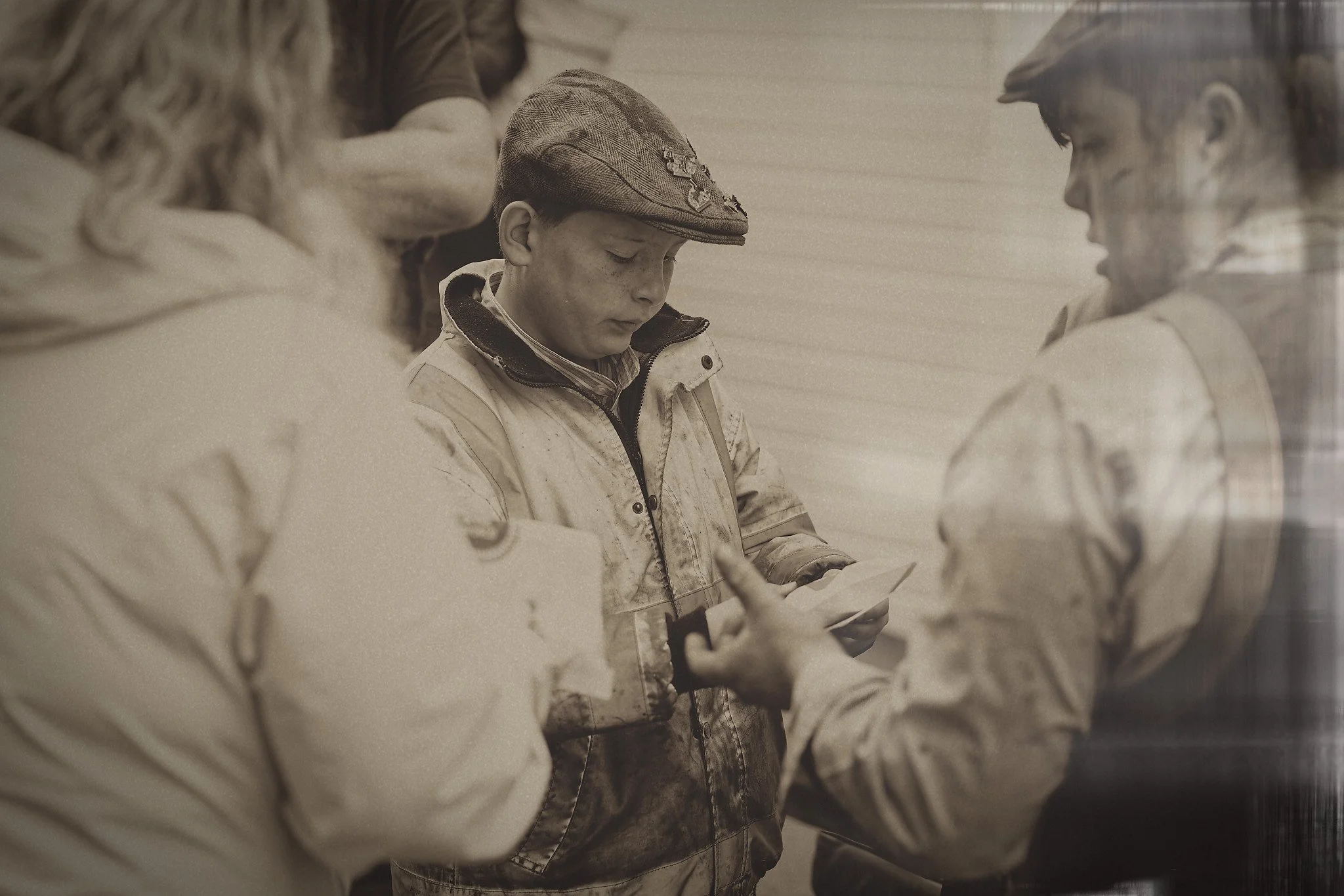 Group of people, including a young man in a cap, gathered around looking at papers in an indoor setting.
