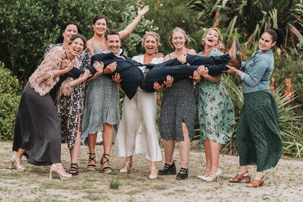 Group of women happily lifting a man in a suit outdoors.