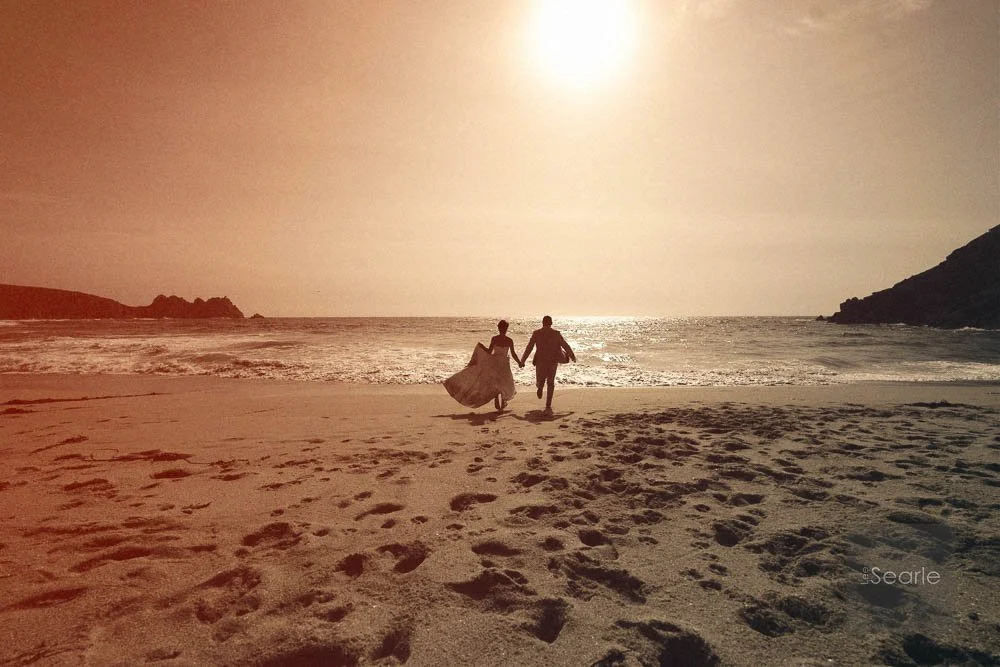 A couple holding hands and walking along the beach at sunset.