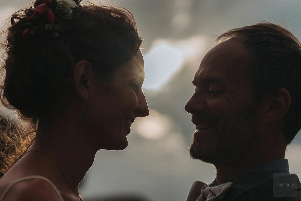 A silhouette of a woman and an older man smiling at each other, close face-to-face, with a cloudy sky in the background.