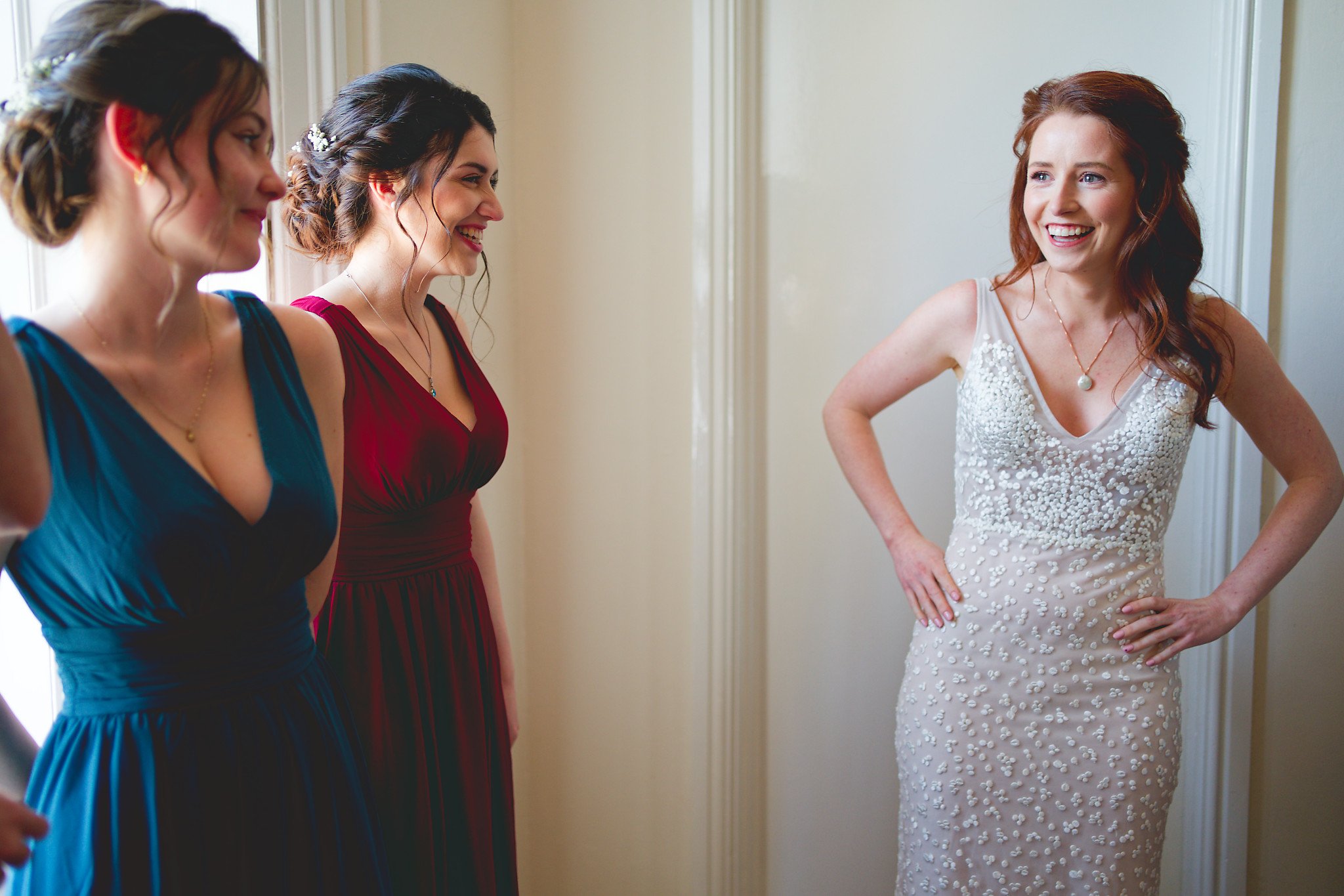 A bride in a white beaded wedding dress laughing with three bridesmaids in colorful dresses.