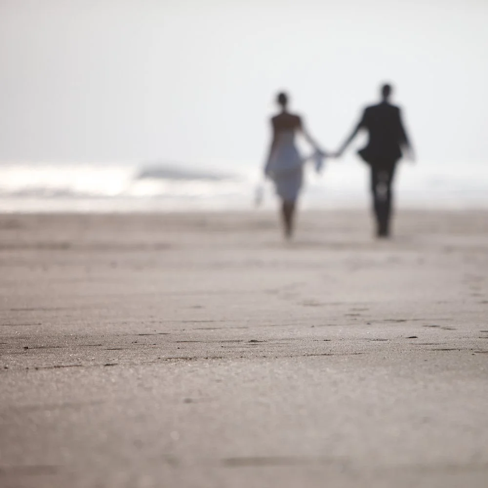 A blurred image of a couple walking hand in hand on the beach during daytime.