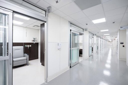 Empty hospital corridor with patient rooms and a waiting area with a gray armchair. Shows construction work done by JJD Matthews, a recipient of the NYS MBE.