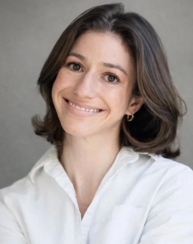 A woman with short brown hair smiling at the camera, wearing a white collared shirt and gold hoop earrings.