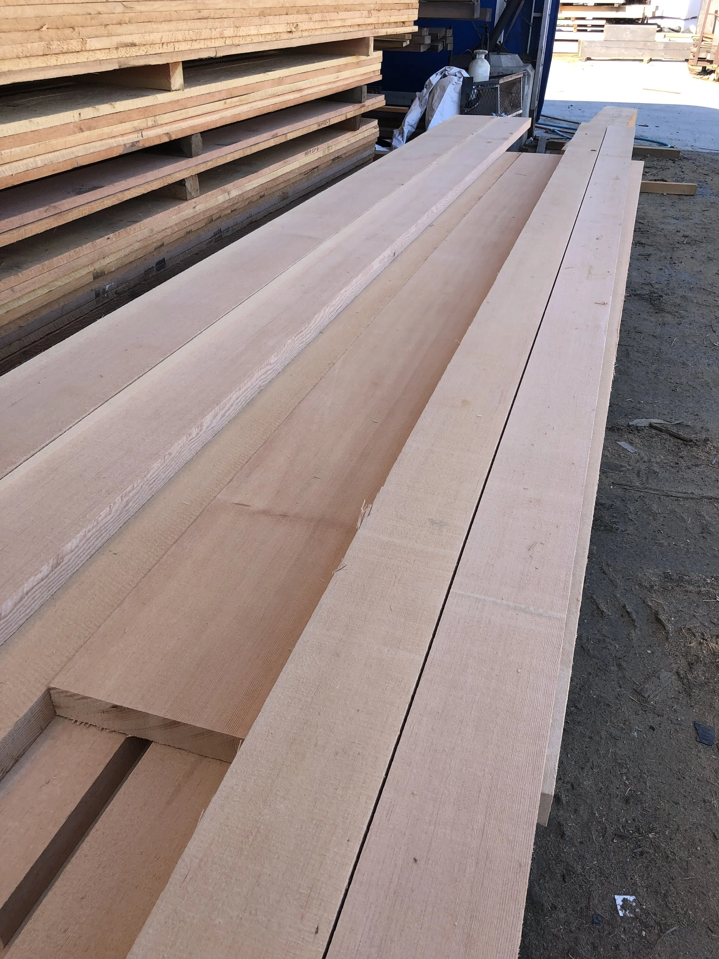 Stack of cut lumber boards stored outdoors at a construction site.