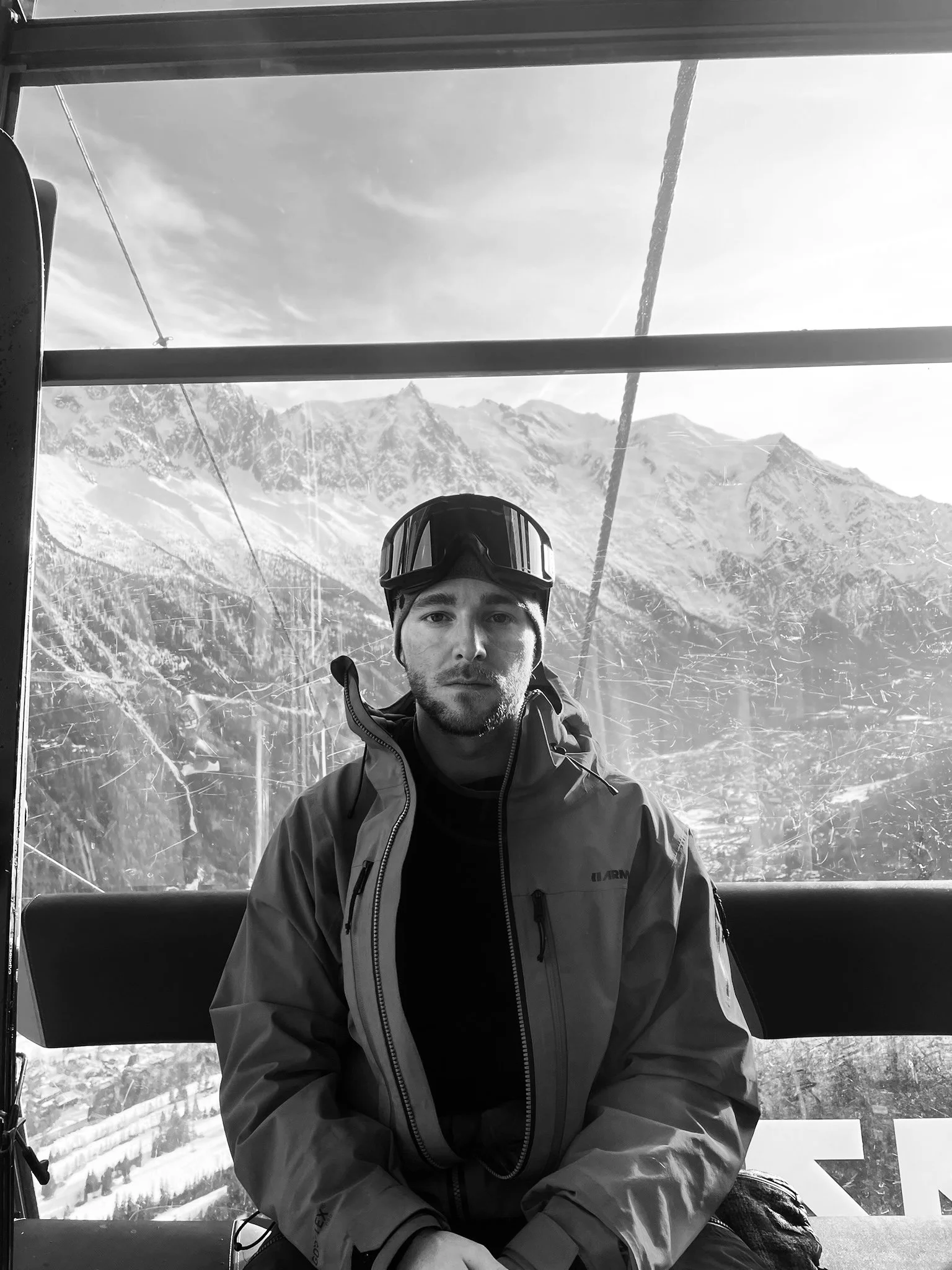 Person in ski gear sitting in gondola with snowy mountain scenery outside.
