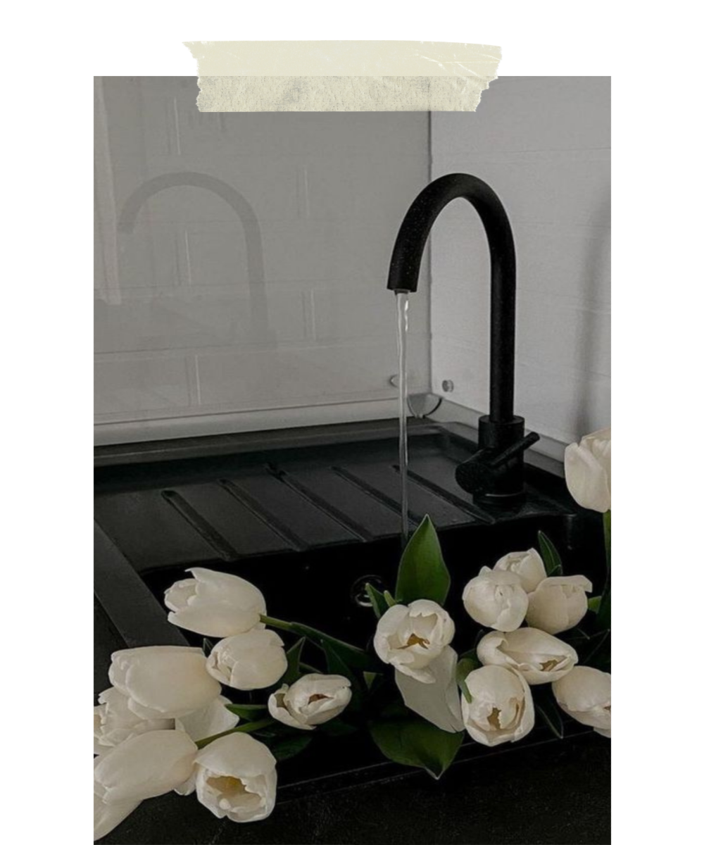 White tulips on a black kitchen sink with a black faucet and running water.
