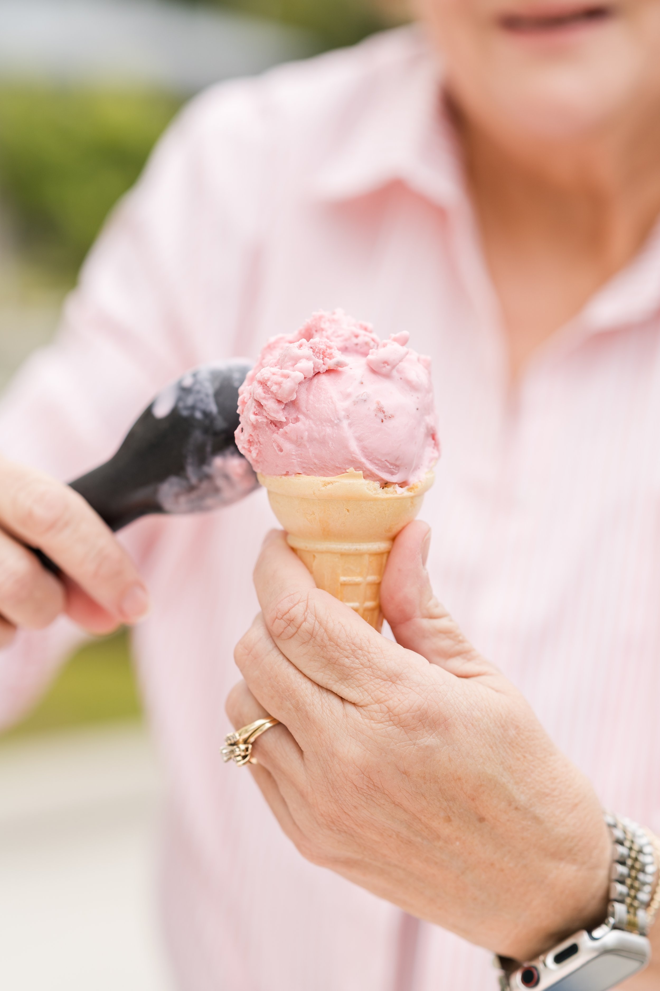 Scooping strawberry ice cream from the cart onto a cone