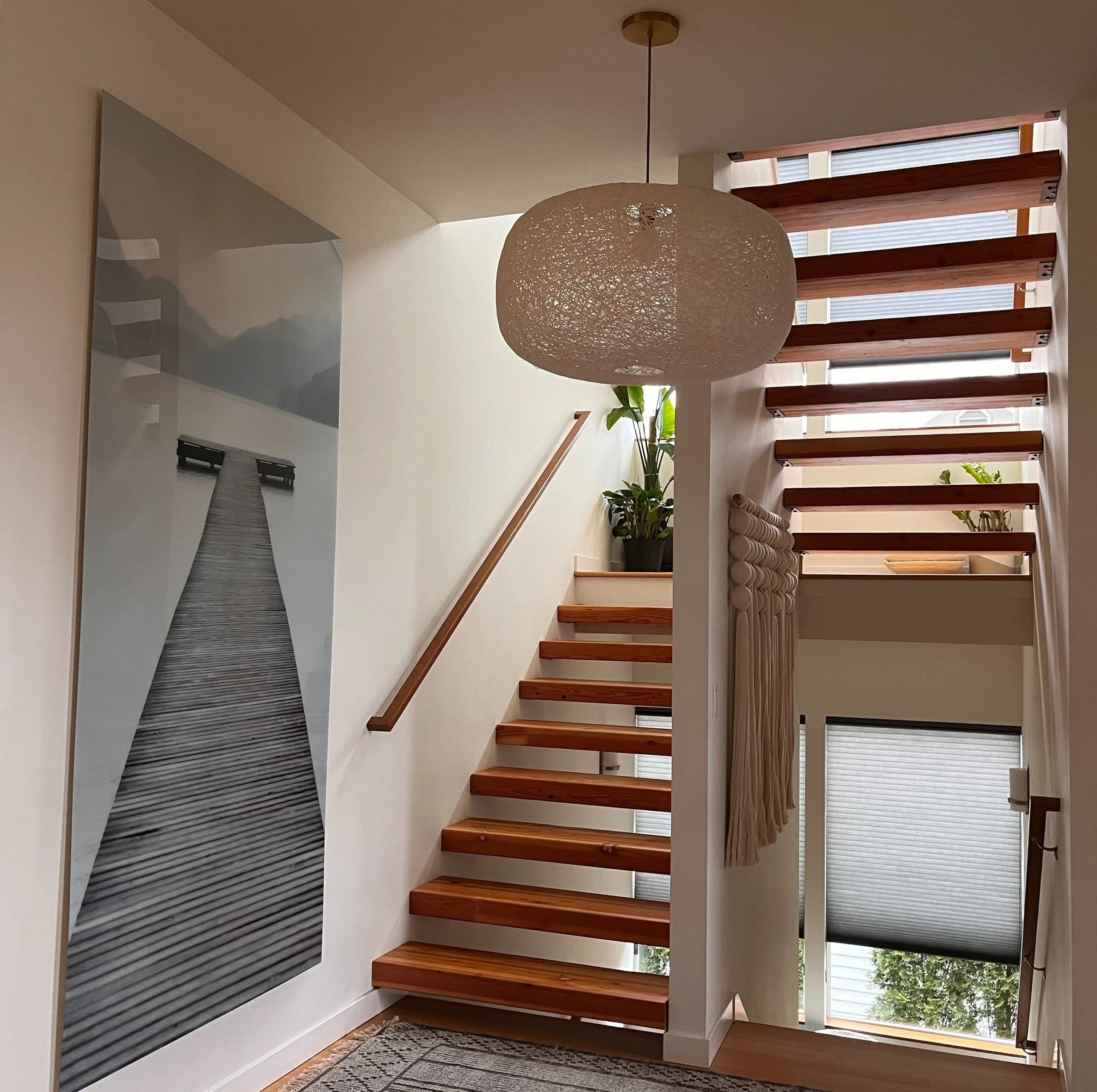 A beautifully designed modern staircase area featuring open wooden treads with metal supports, creating a floating stair effect that enhances the light and airy feel of the space. A large vertical photograph of a serene dock stretching into misty wat