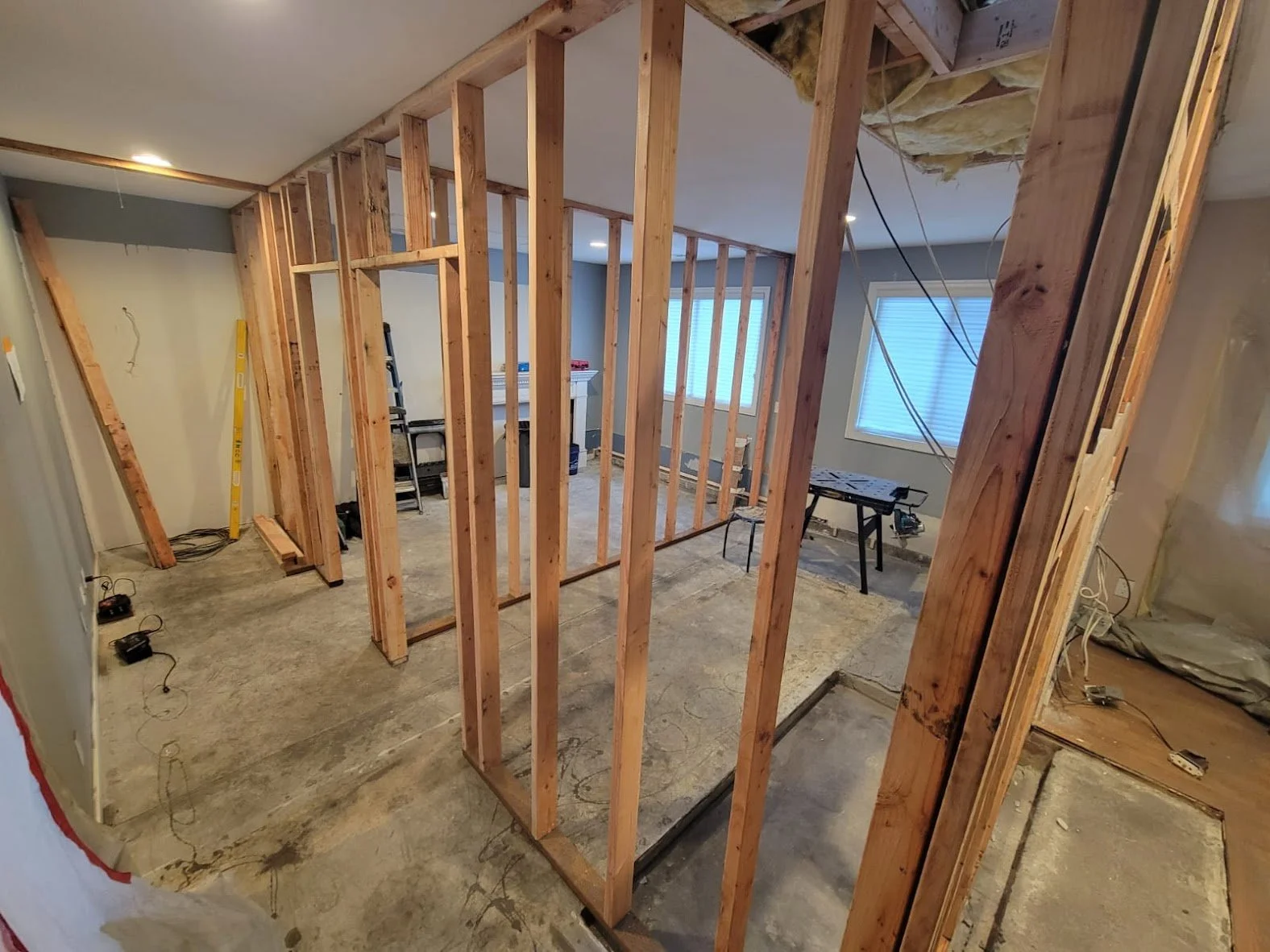 This image captures a different angle of the same residential interior construction project, showing the newly framed partition walls from a corner perspective. The open ceiling area in the foreground reveals exposed insulation and wiring, indicating