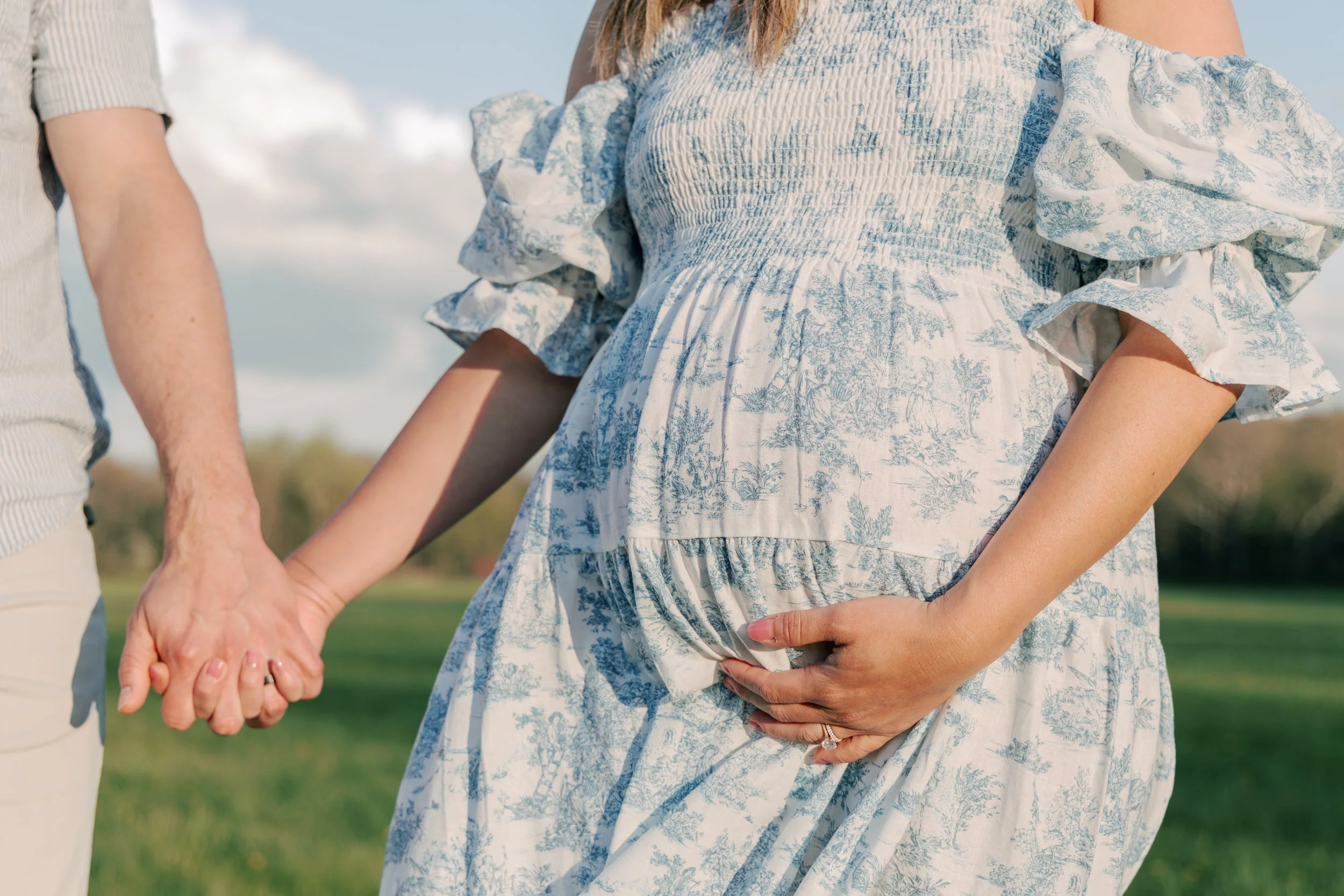 Close-up of pregnant woman holding hands with her partner, focus on her baby bump and both hands intertwined.