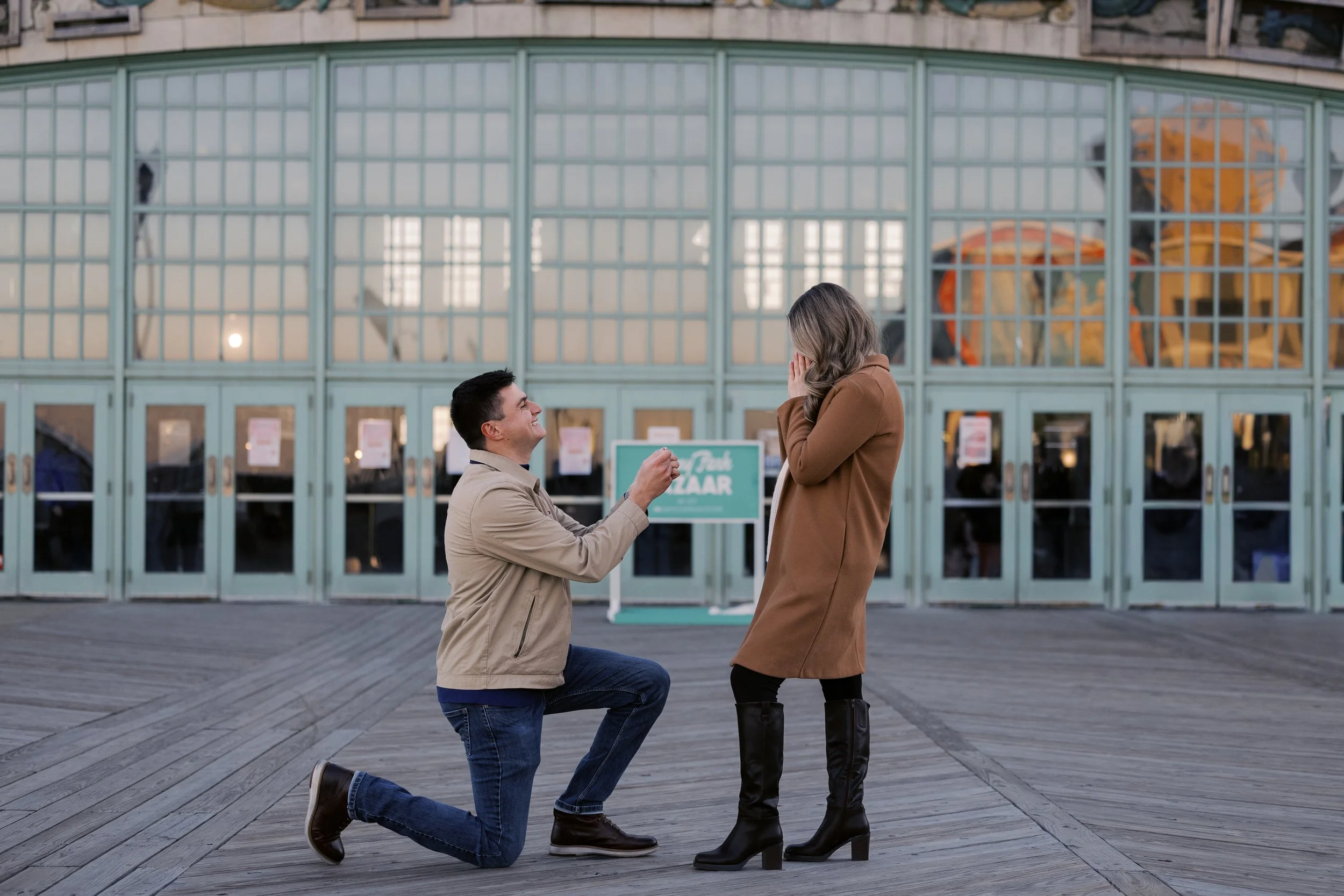 A smiling couple walking hand in hand along a beach, with houses in the background under a clear sky.