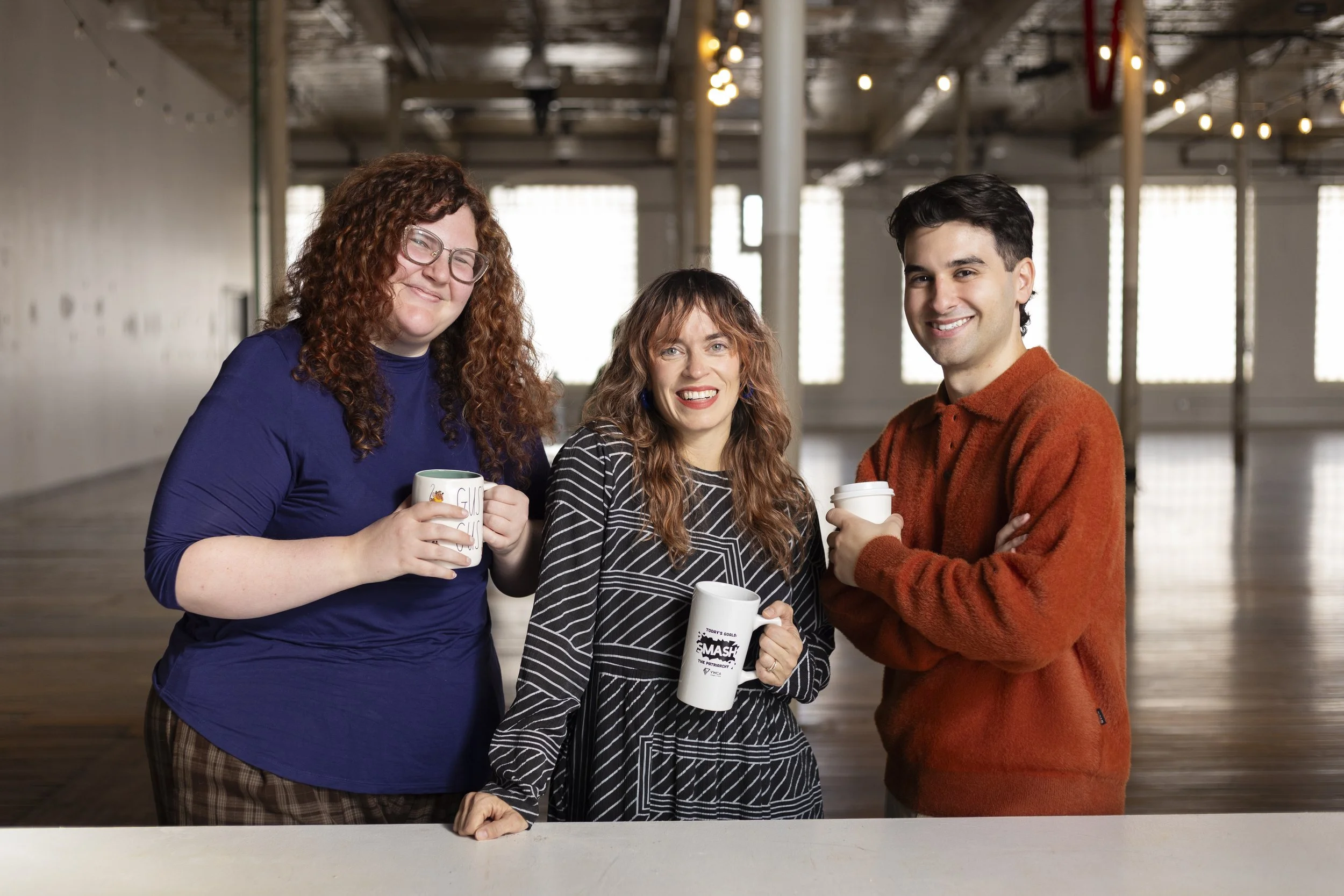 a photograph of three people smiling and holding mugs