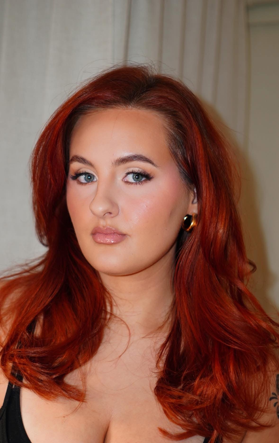 Portrait of a woman with red hair, blue eyes, and earrings, looking at the camera.