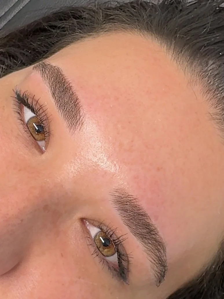 Close-up of a woman's face showing her brown eyes, well-groomed eyebrows, and smooth skin with slight redness.