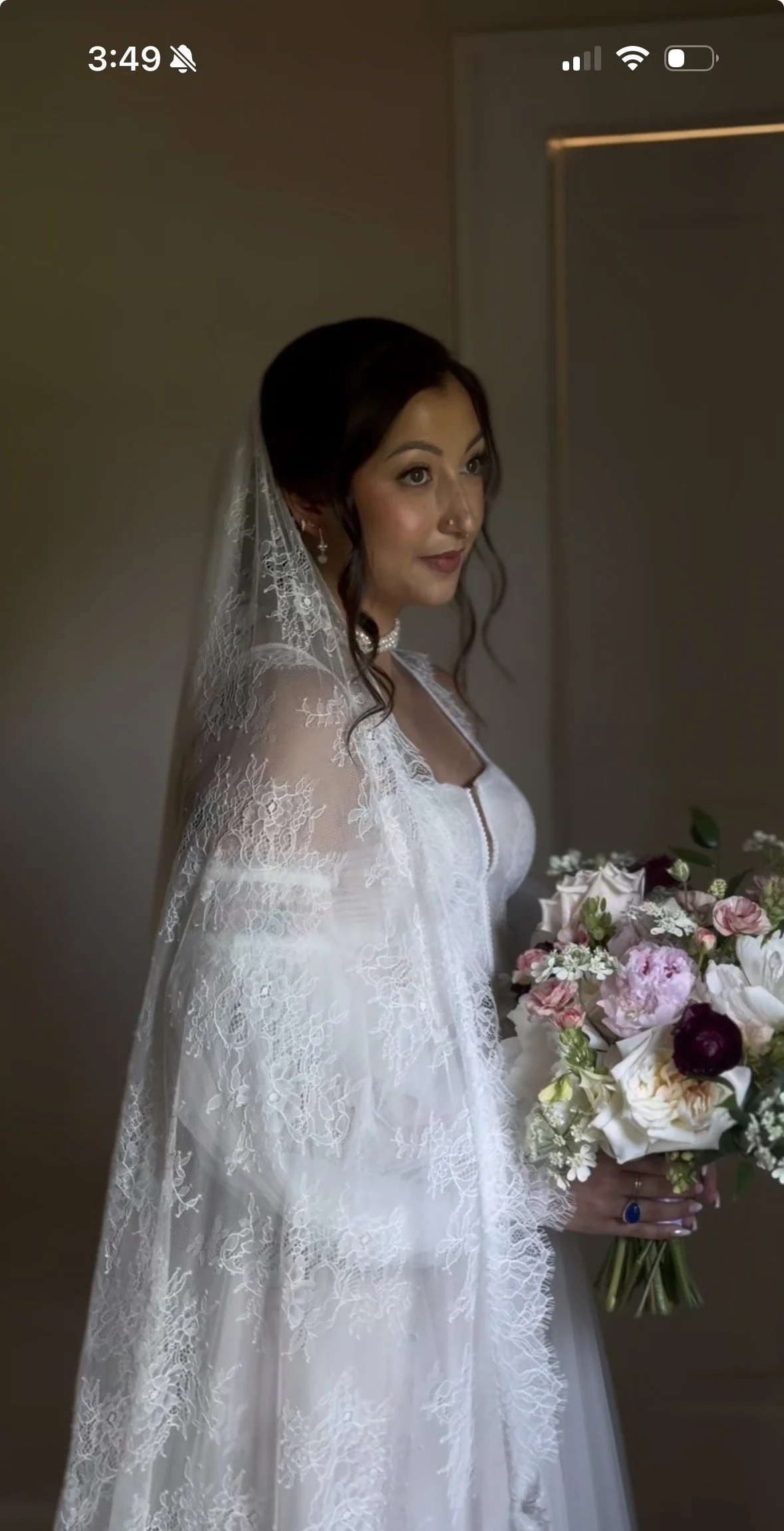 Bride in a white lace wedding dress holding a bouquet of pink, white, and dark red flowers.