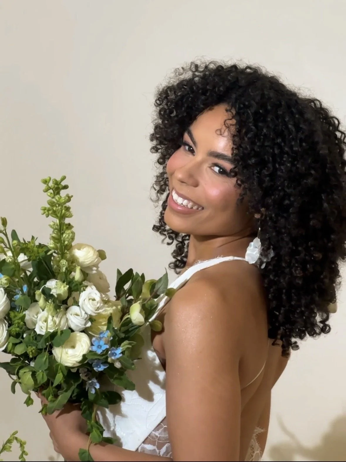 A woman with curly hair smiling while holding a bouquet of white and green flowers