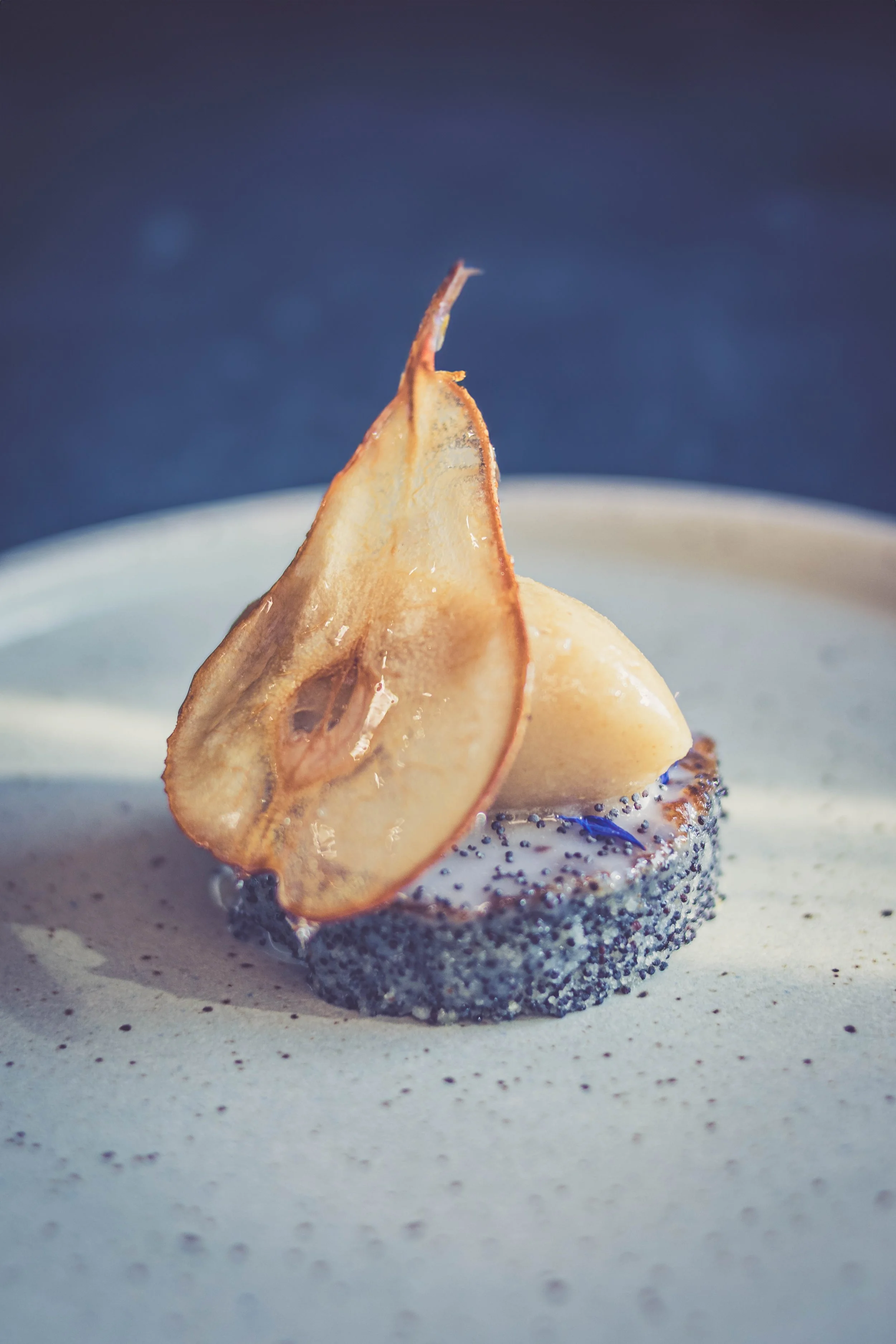 Une tranche de poire séchée posée sur un dessert à base de pavot sur une assiette.