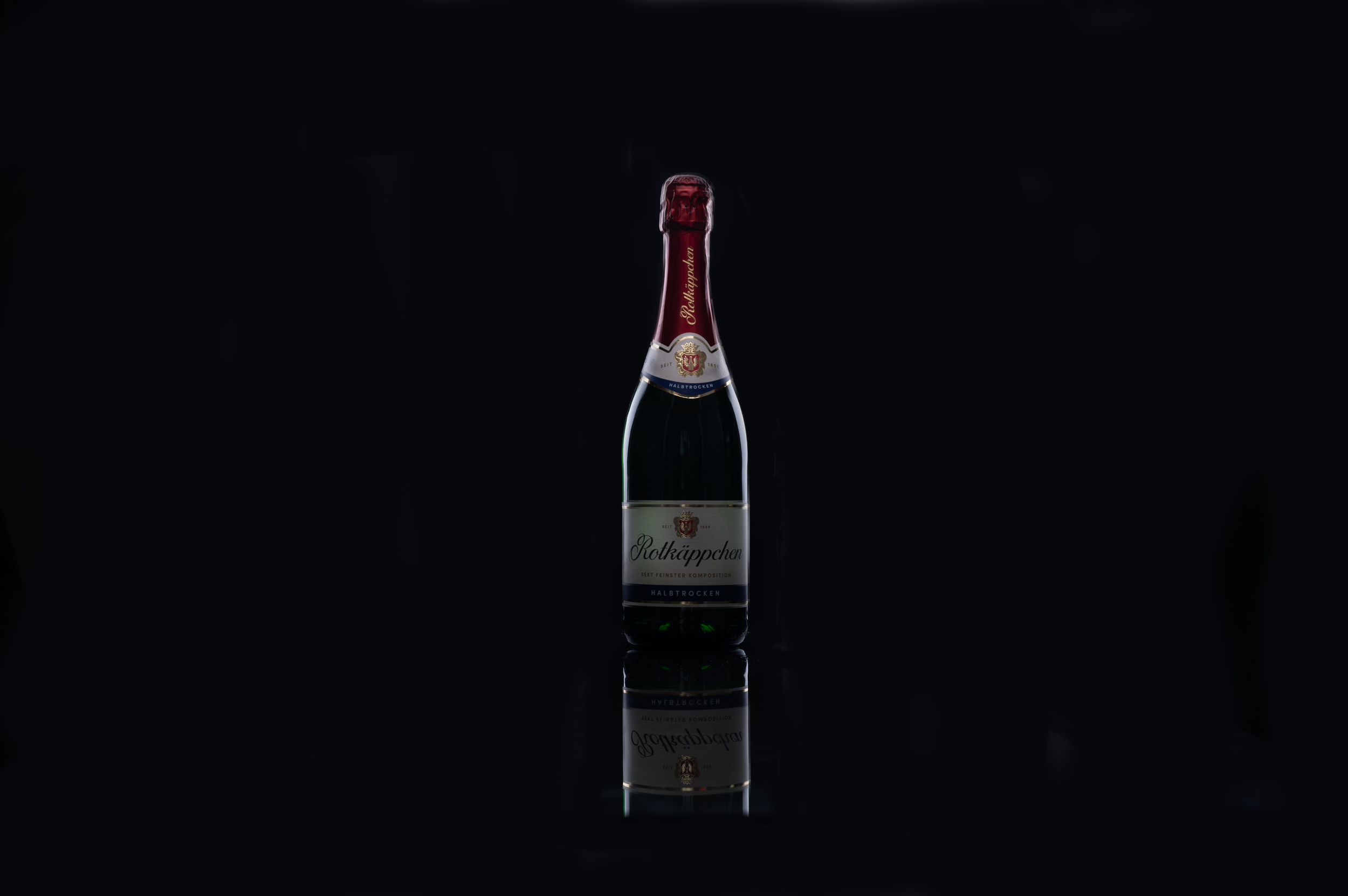 A dark background with a single bottle of Rotkäppchen sparkling wine centered, reflections visible on the surface below.