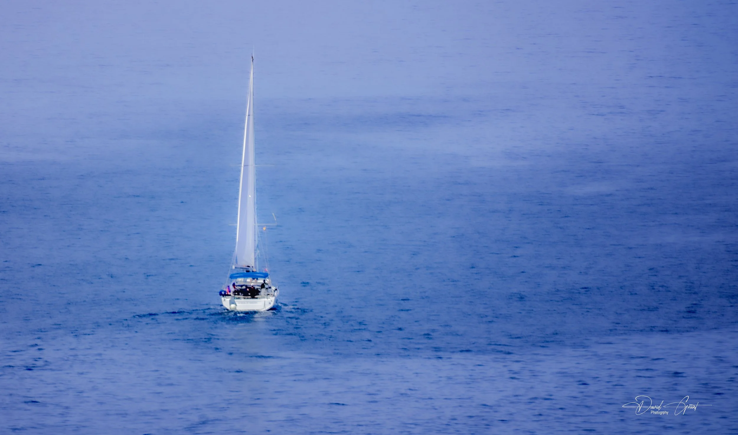 A sailboat with a tall mast on a calm, blue body of water.