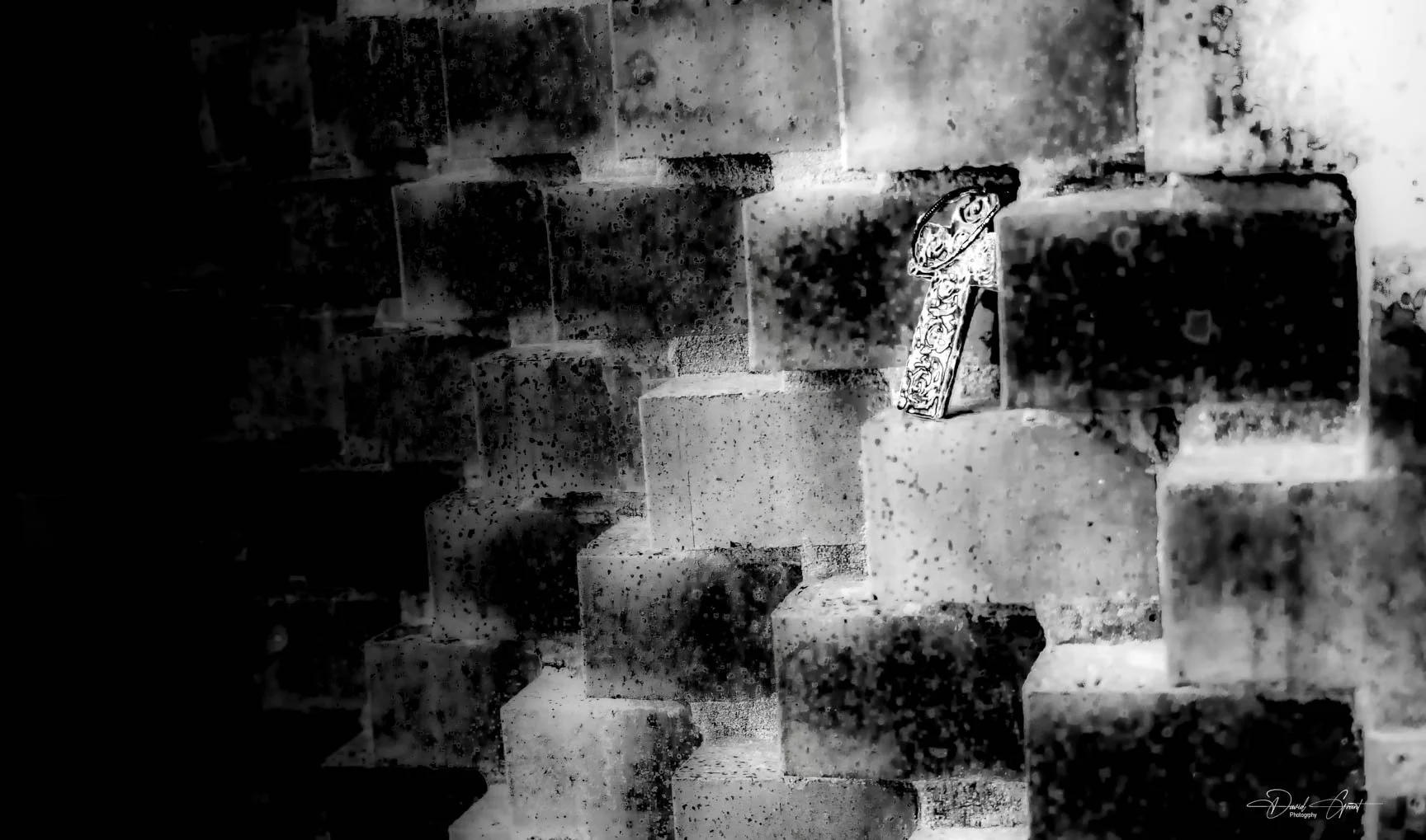 A black and white photograph of a brick wall with a decorative letter 'A' attached to it.