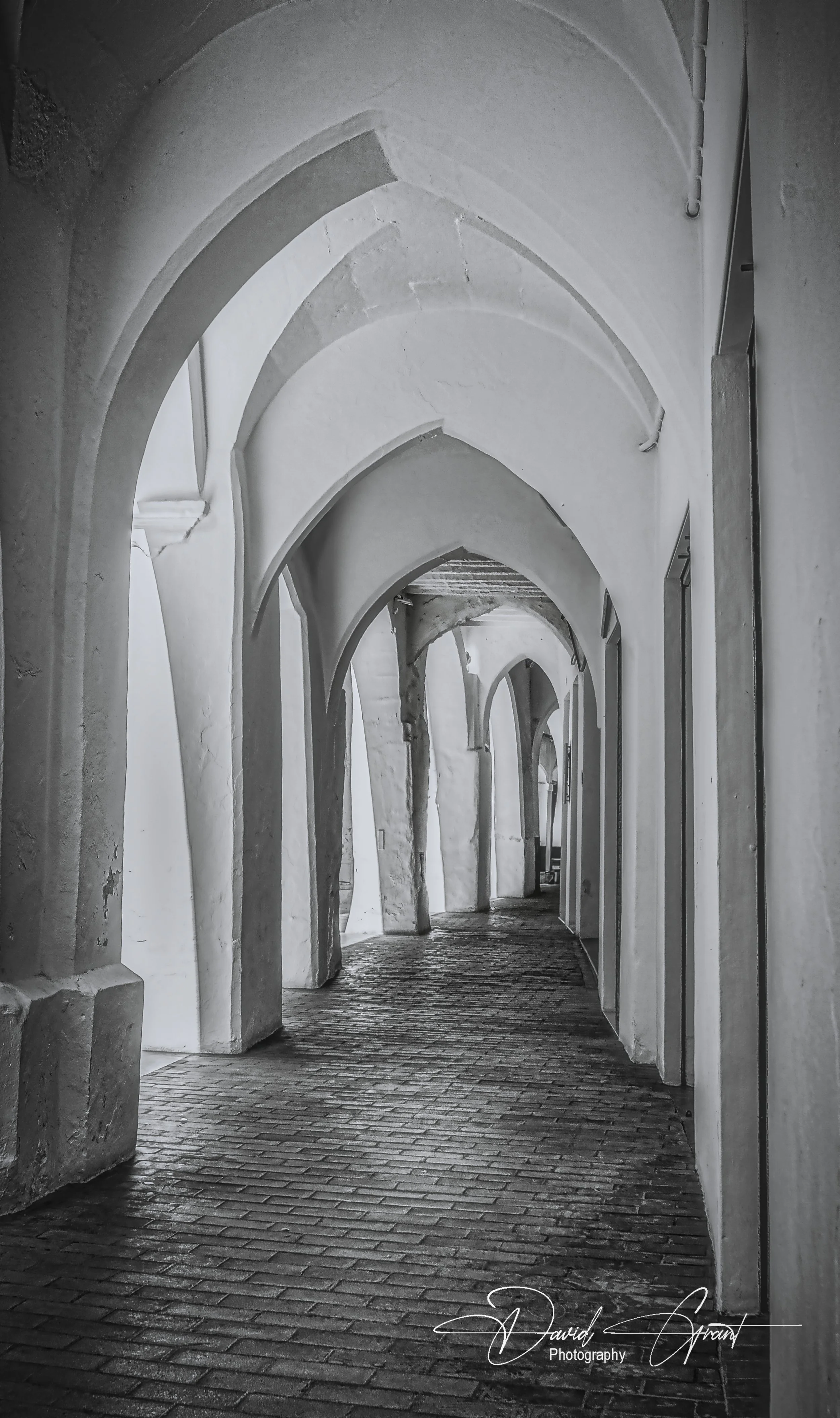 A corridor with arched white walls and ceiling, featuring a cobblestone floor and a series of arches receding into the distance.