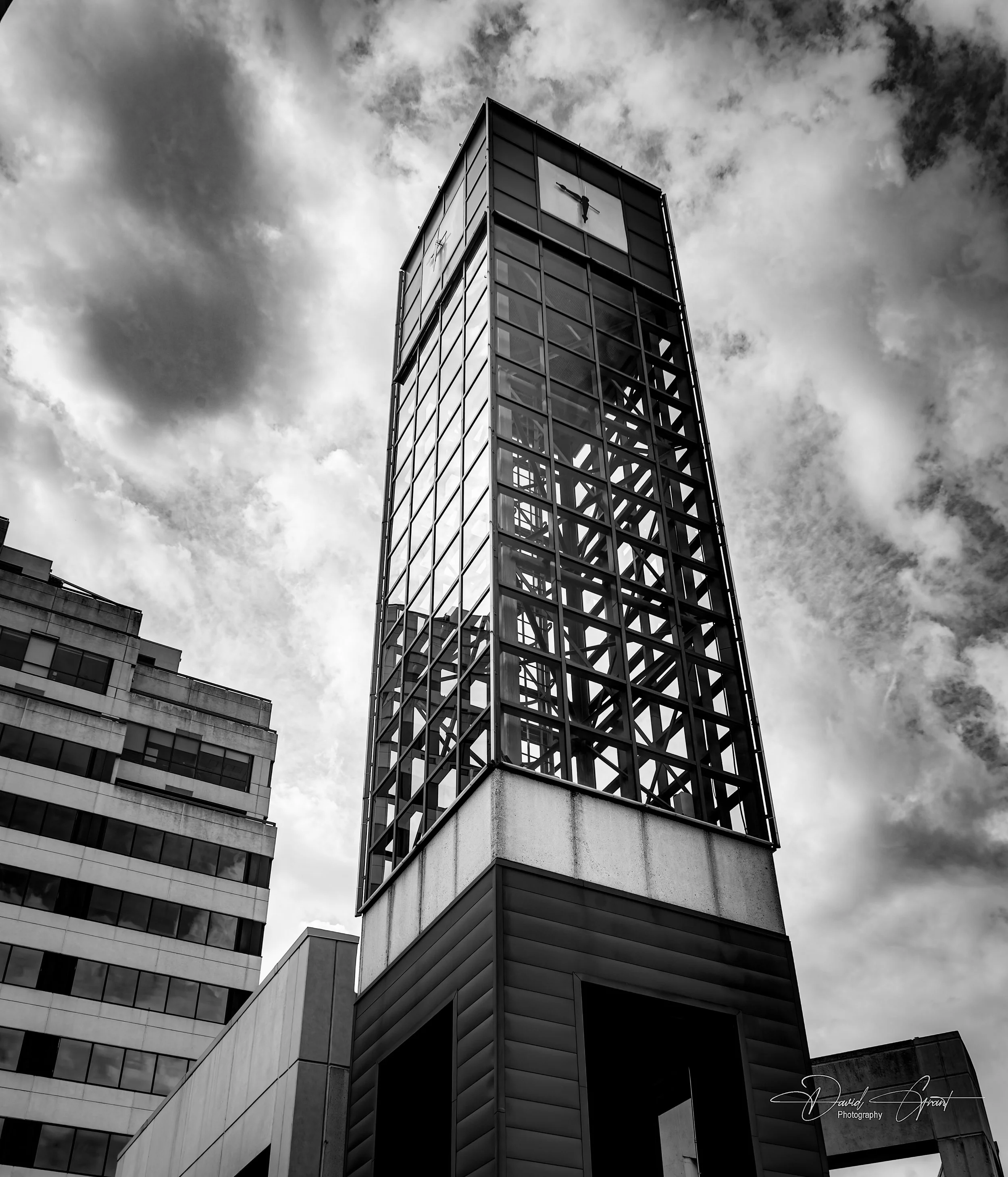 Black and white photo of a tall skyscraper with a glass and steel frame, featuring visible structural beams, against a cloudy sky.