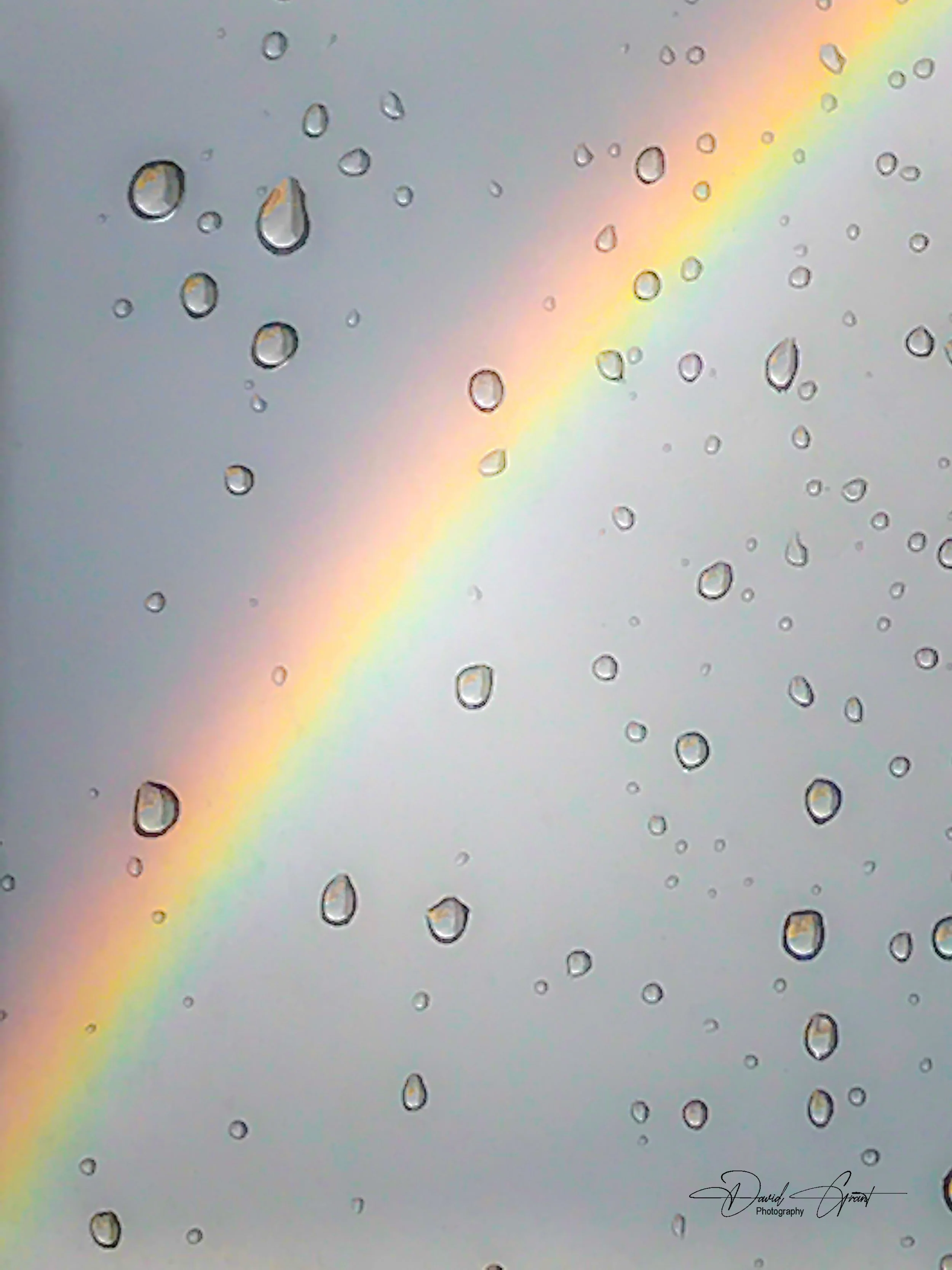 Drops of water on a transparent surface with a rainbow in the background.