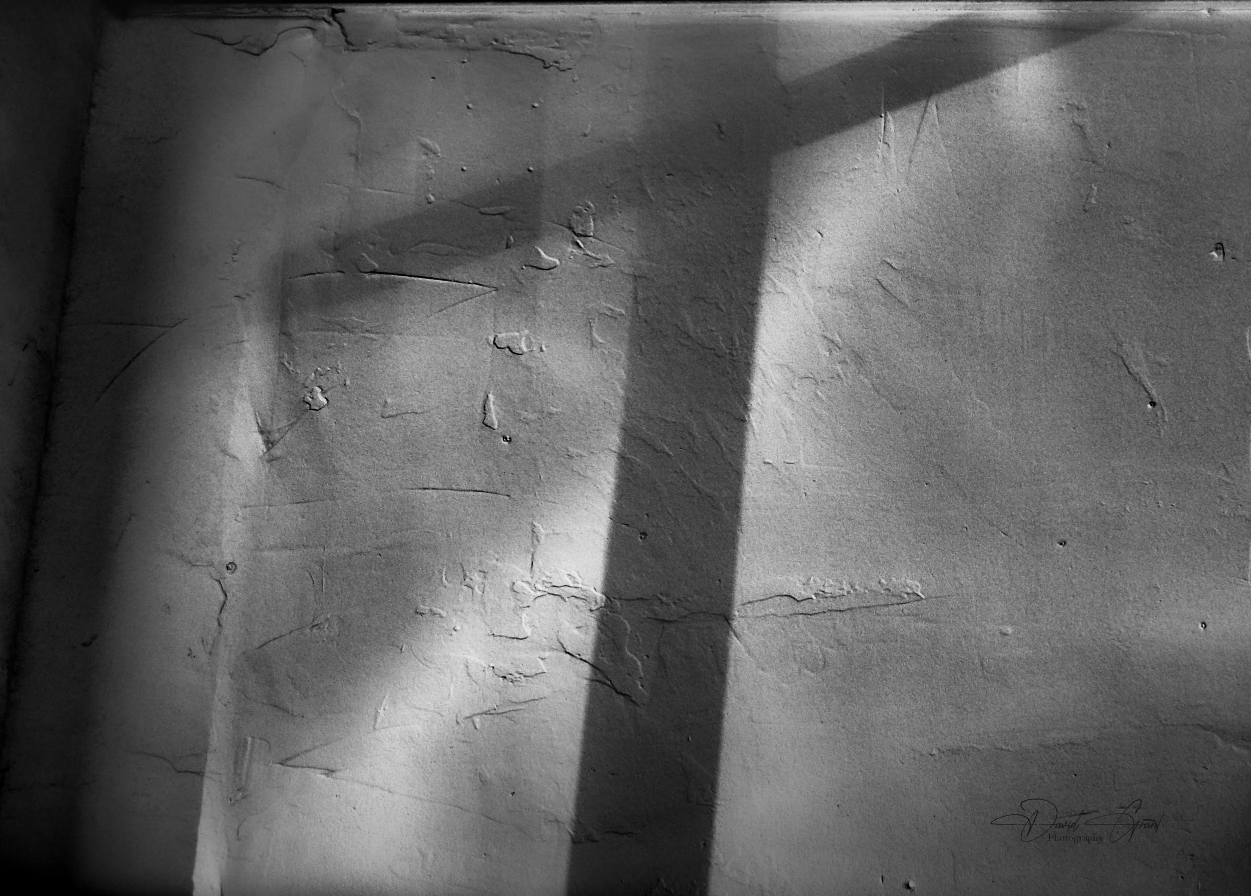 Close-up of a textured wall with cracks, shadows, and peeling paint in black and white.