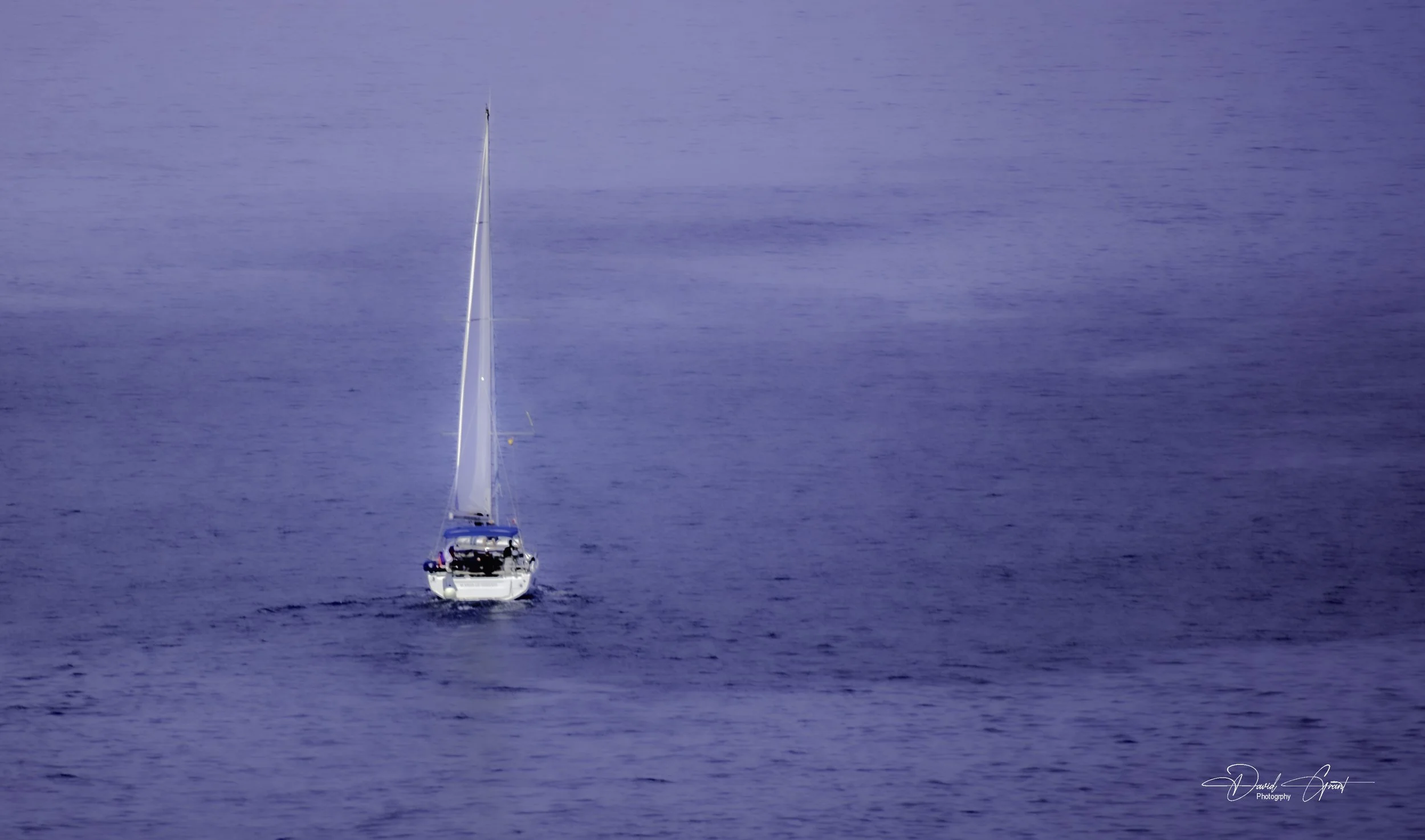 A sailboat with a tall mast sailing on calm blue ocean water.