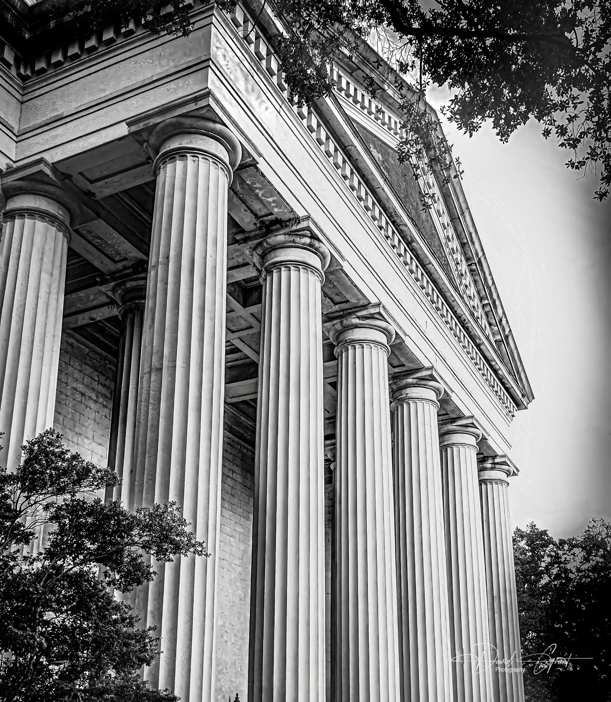 Black and white photograph of a classical building with tall, fluted columns and ornate detailing, surrounded by trees.