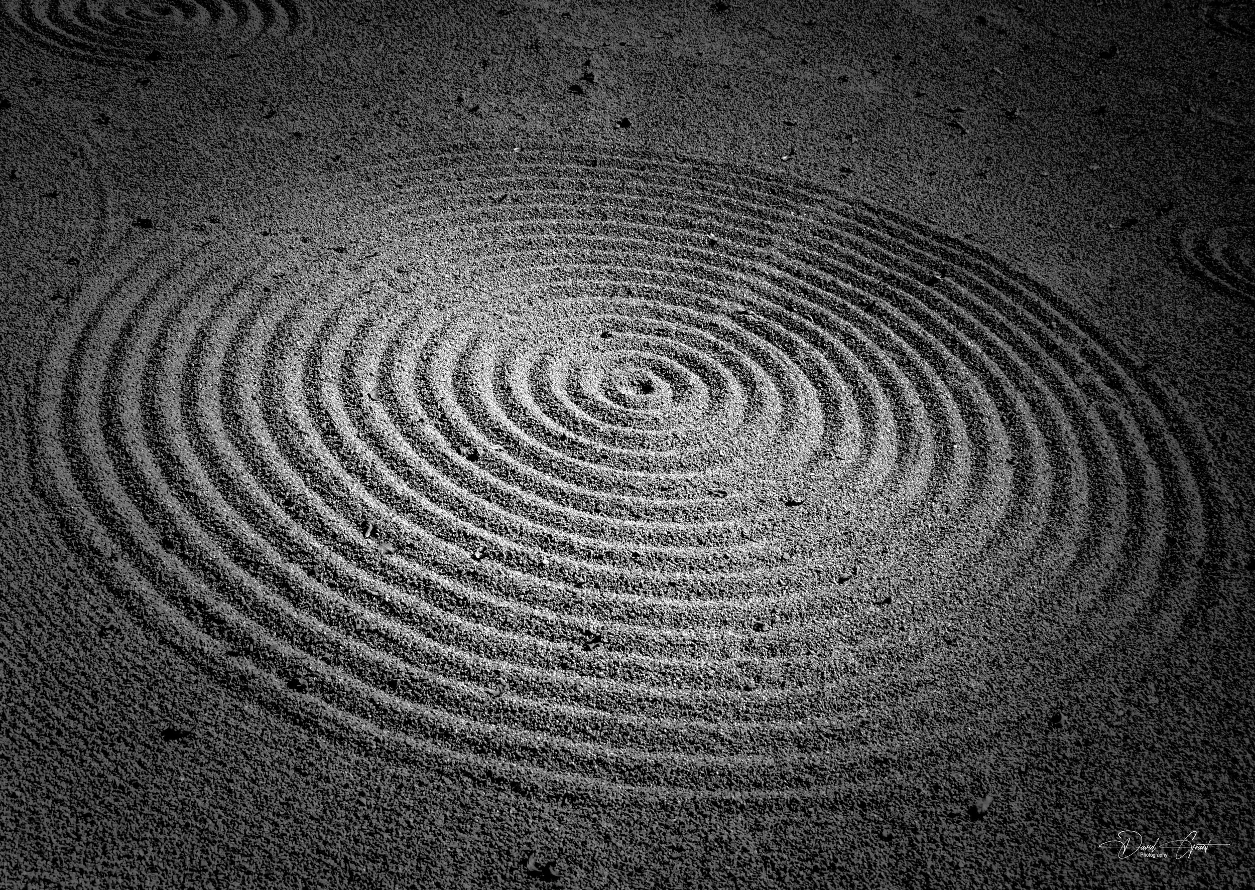 Close-up of a sand surface with concentric circular ripples, creating a textured pattern.