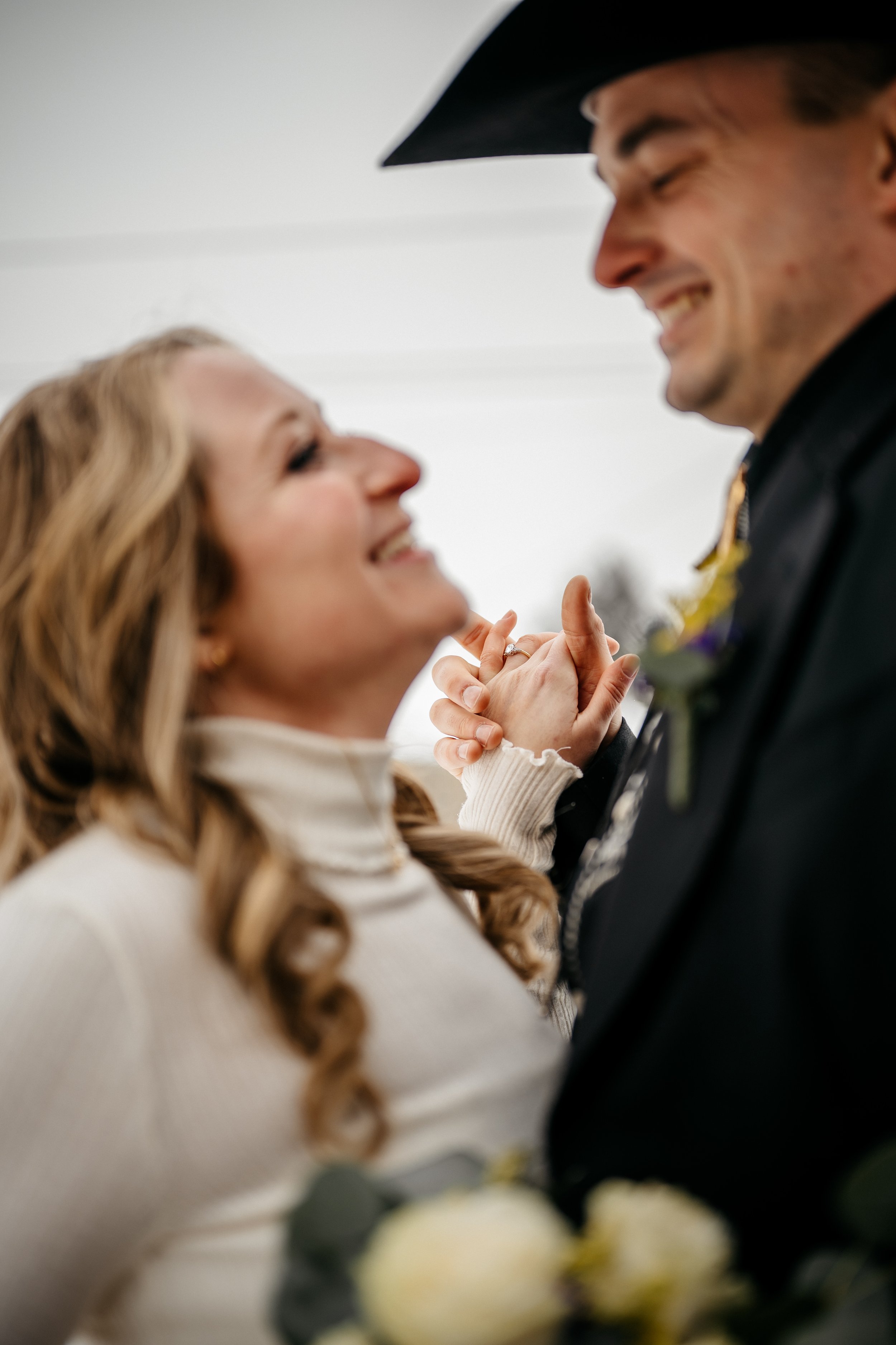 A Dayton Ohio bride and groom with a cowboy hat smiling and holding hands showing their rings during their wedding ceremony.