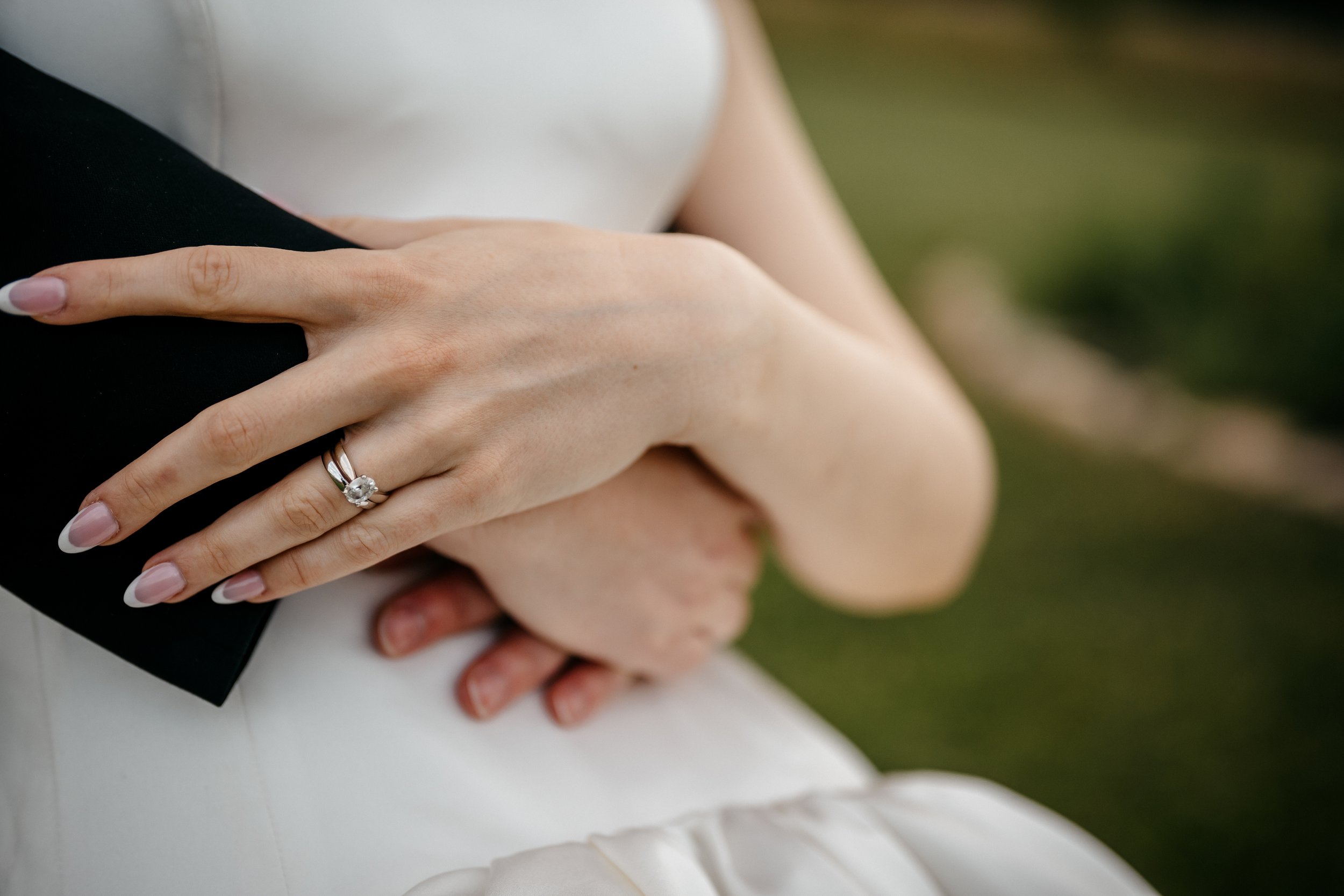 Close-up of a Dayton Ohio bride's hand with her wedding ring on the ring finger, resting on her grooms hand, outdoors with blurred greenery in the background.