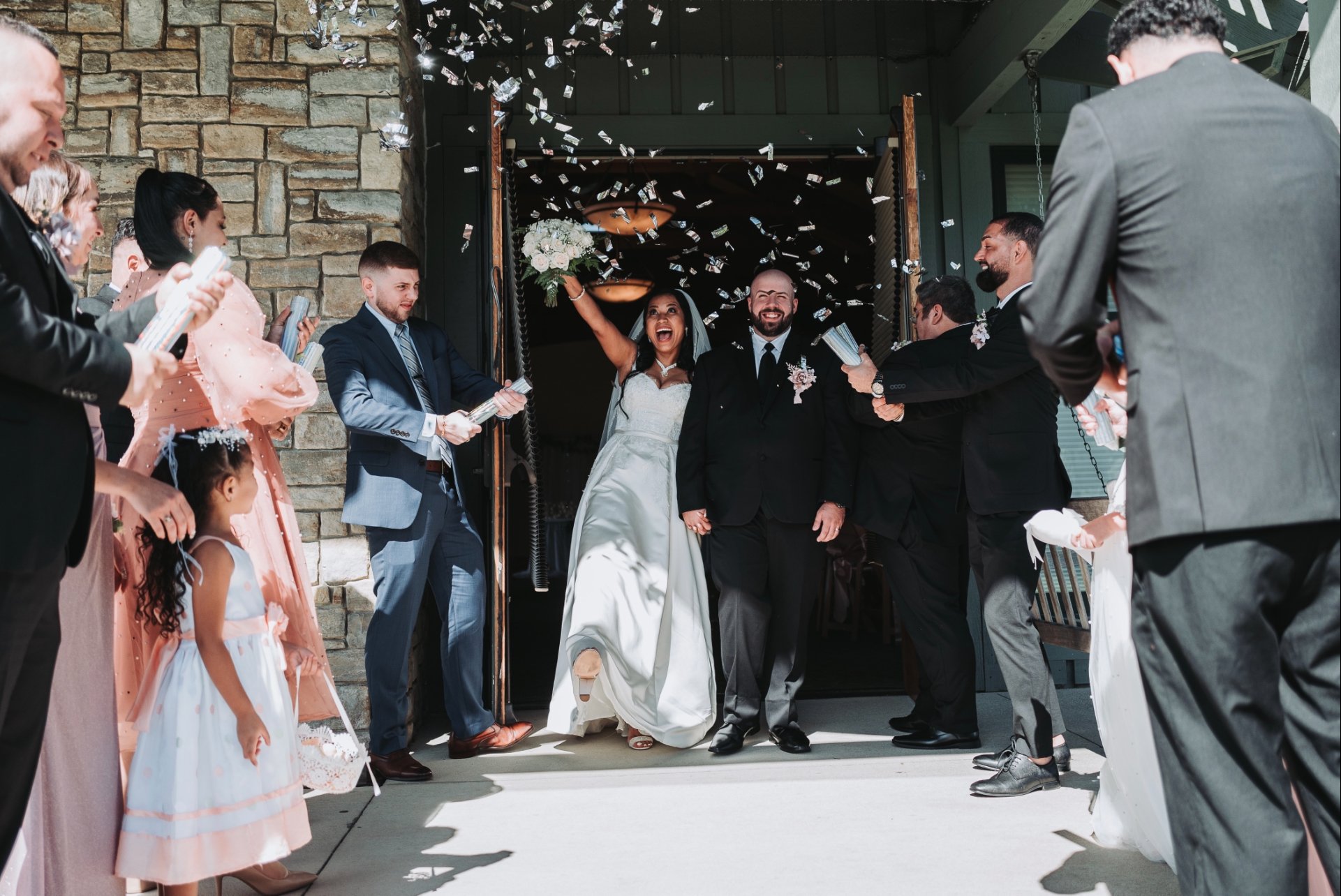 Bride and groom exiting a building in Dayton Ohio surrounded by friends and family, celebrating with confetti.