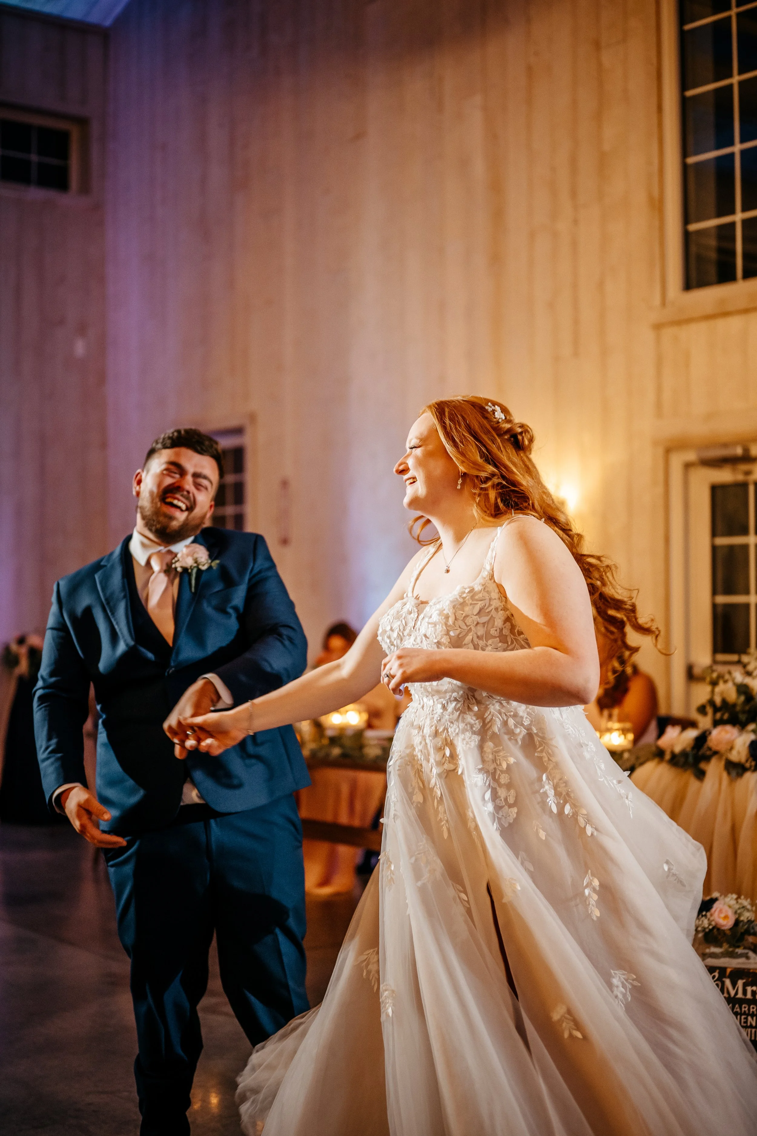 A Dayton Ohio bride in a wedding dress and a groom in a suit dancing their first dance and laughing at their wedding reception in a decorated hall.