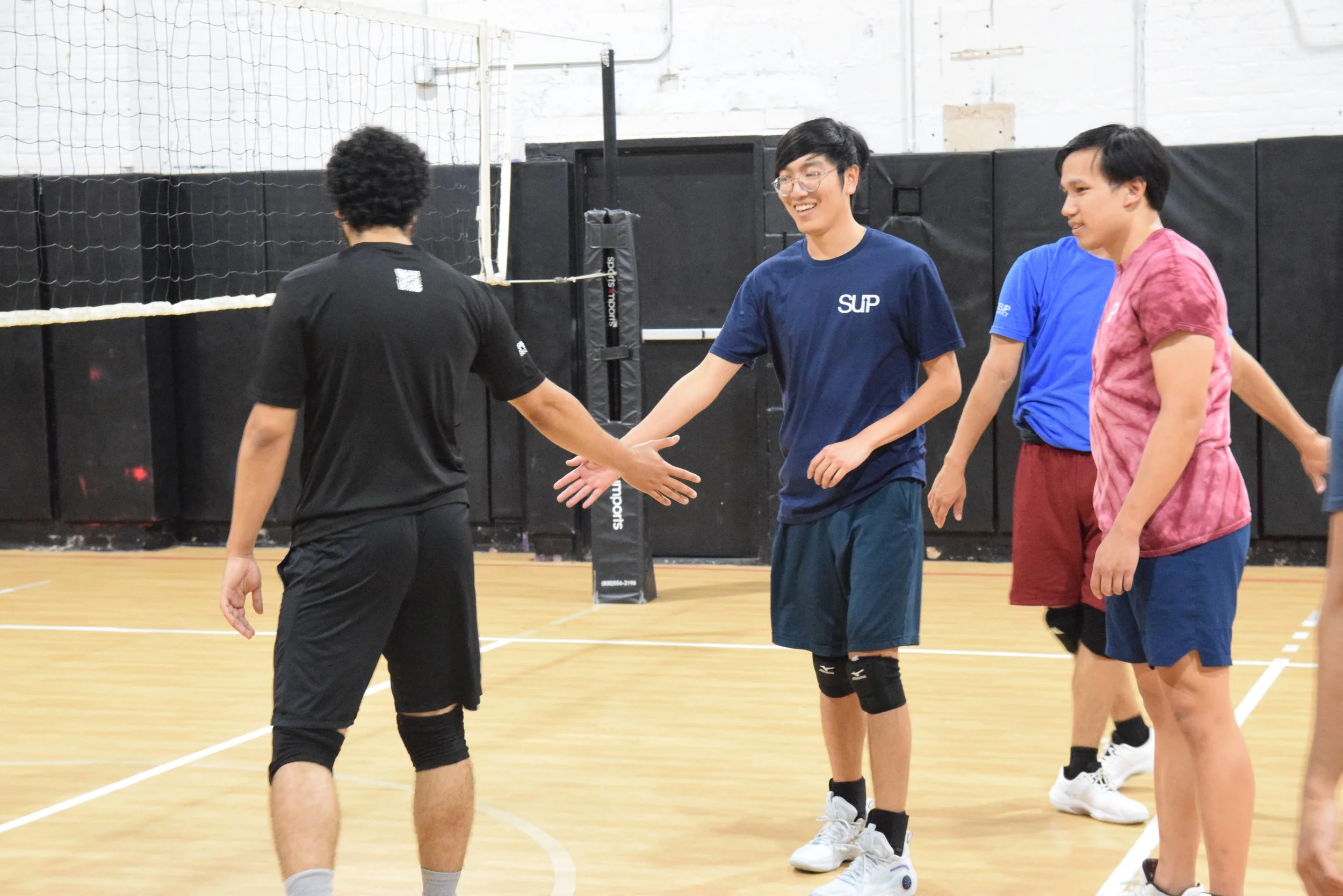 People playing volleyball in an indoor gym, shaking hands after a game
