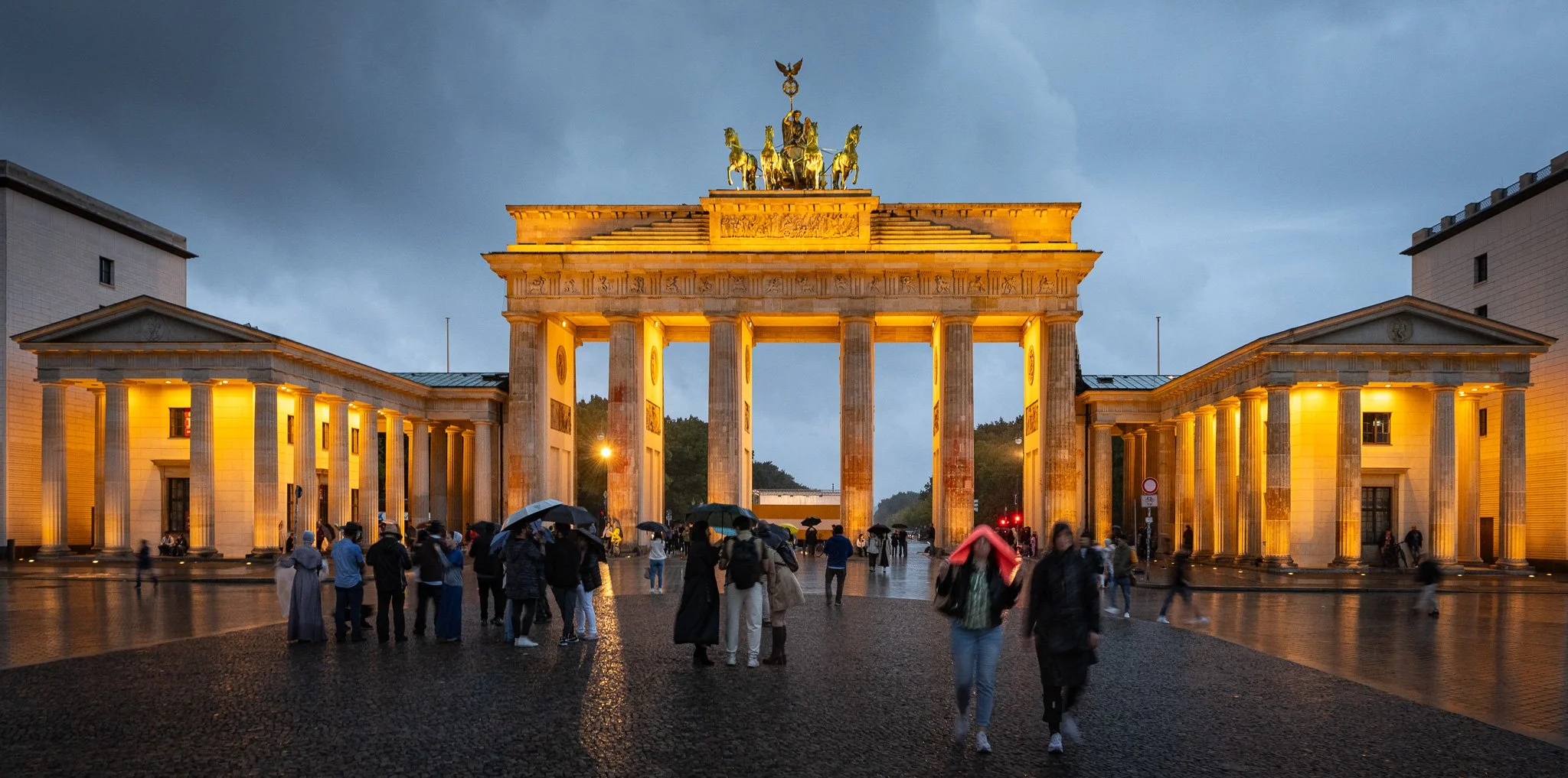A rainy night in Berlin with the Brandenburg Gate bathed in warm light against the cool grayblue sky.