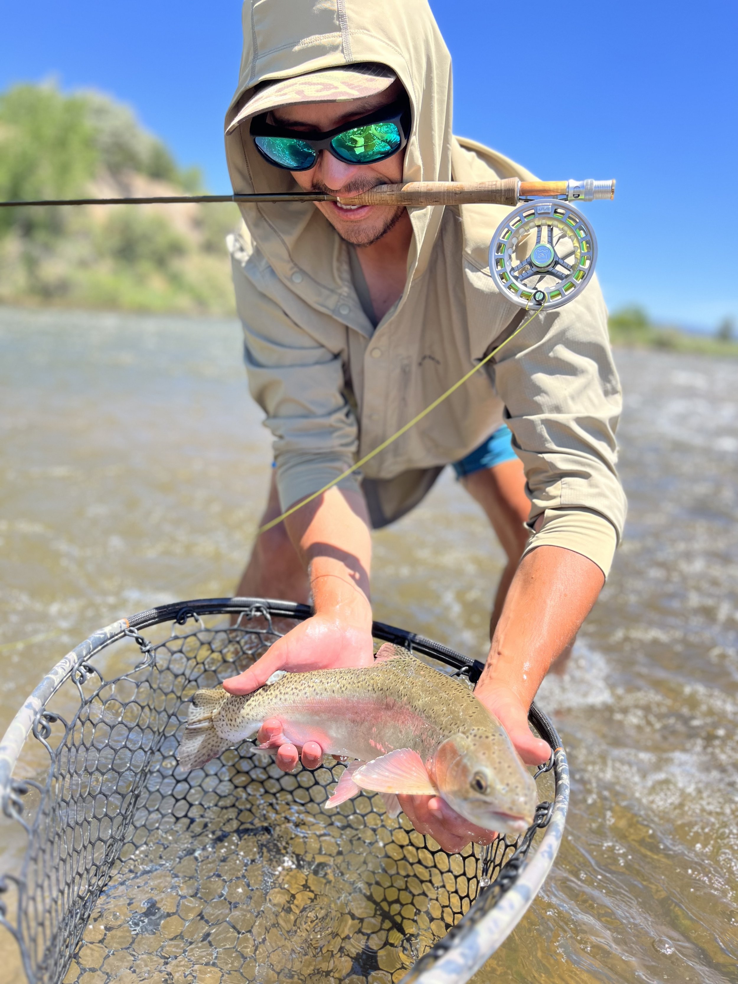 Angler holding a rainbow trout in a net while fly fishing in a river.