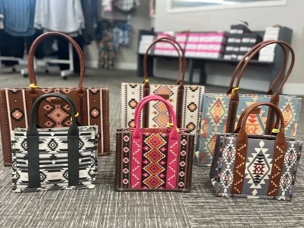 Six small handbags with colorful tribal patterns, displayed on a table in a retail store.