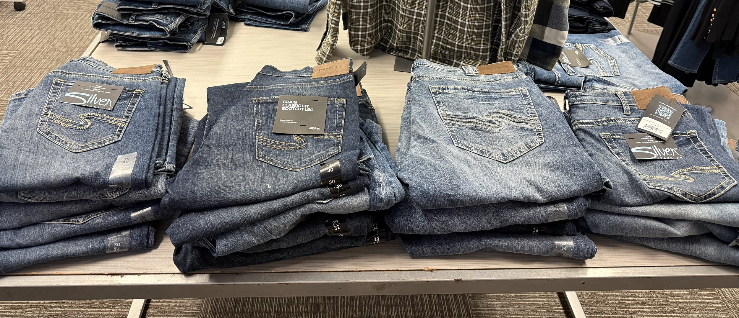 Multiple stacks of folded blue jeans on a display table at a retail store.