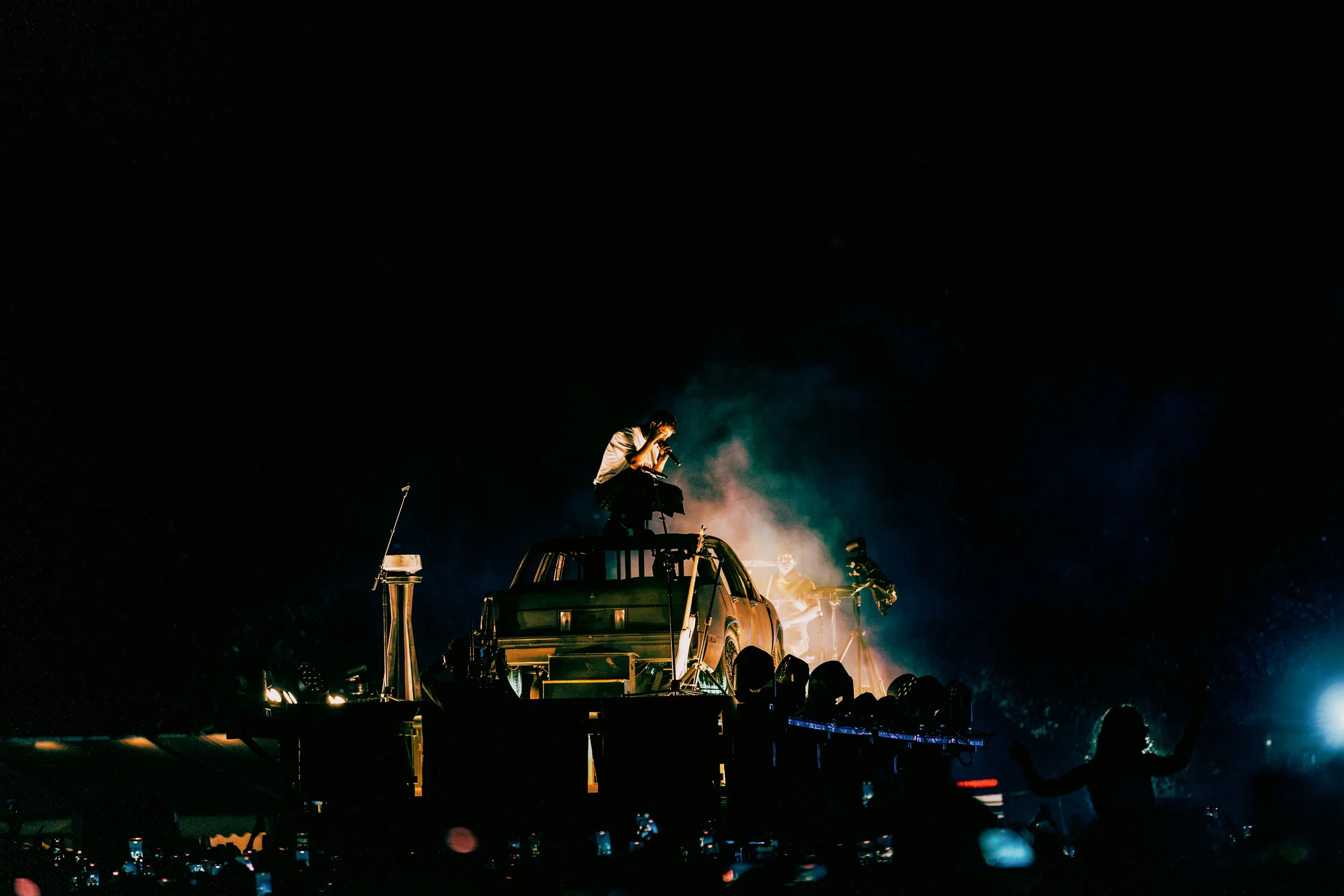 Twenty One Pilots performing at All Points East festival in Victoria Park, London in 2026, on top of a vehicle during night-time with fireworks and bright lights in the background.