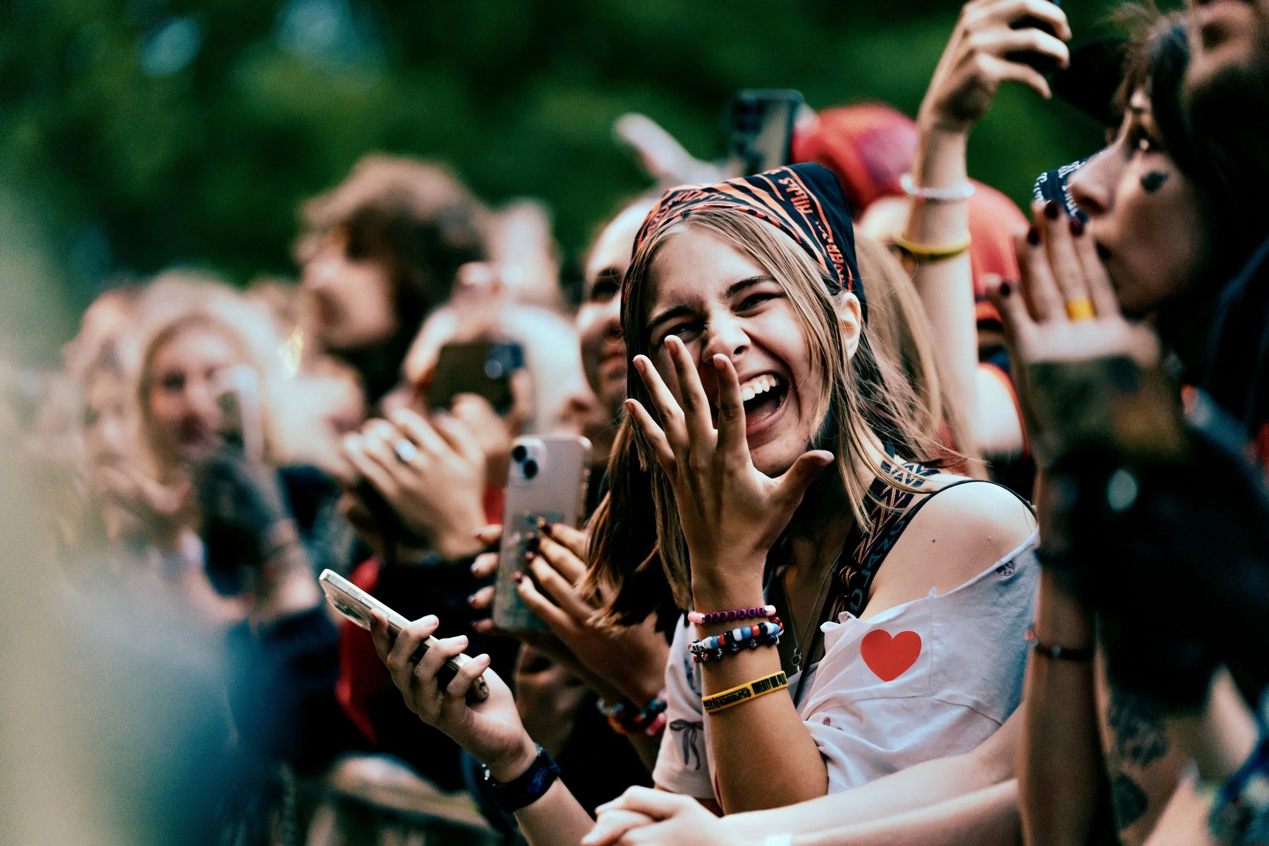 A young woman with long hair and multiple colorful bracelets laughing and taking photos at the barrier of Twenty One Pilots performing at All Points East festival in Victoria Park, London, 2026