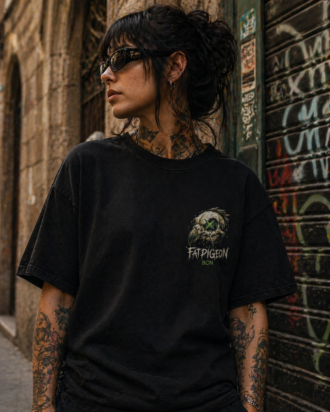 Black oversized streetwear t-shirt featuring small left chest graphic of a cracked pigeon skull with neon green X eye and Fat Pigeon BCN logo in white and green text.