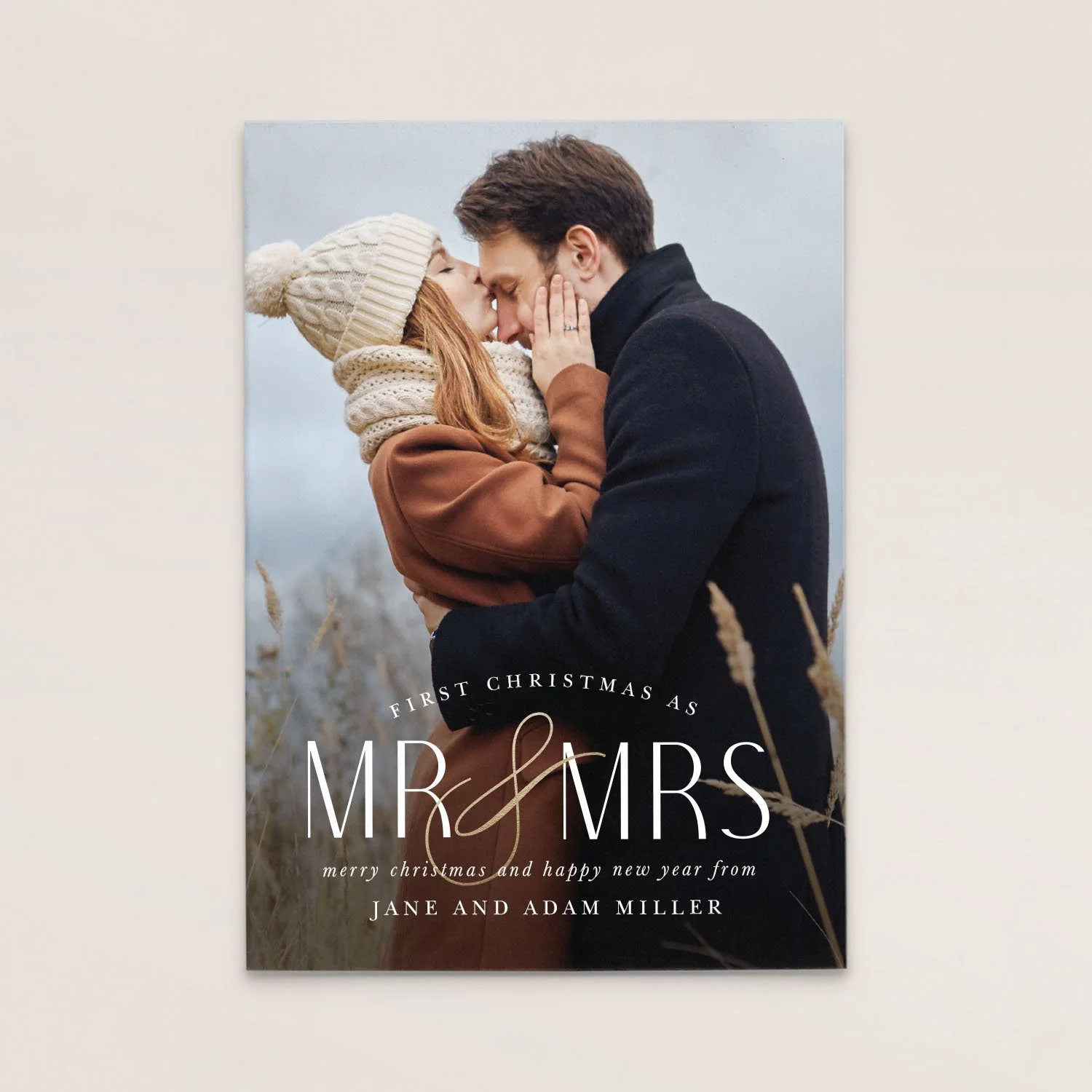 A romantic photo of a couple dressed warmly, touching foreheads and holding each other outdoors. The image is part of a Christmas card that says 'First Christmas as Mr & Mrs,' with a message wishing Merry Christmas and Happy New Year from Jane and Ad