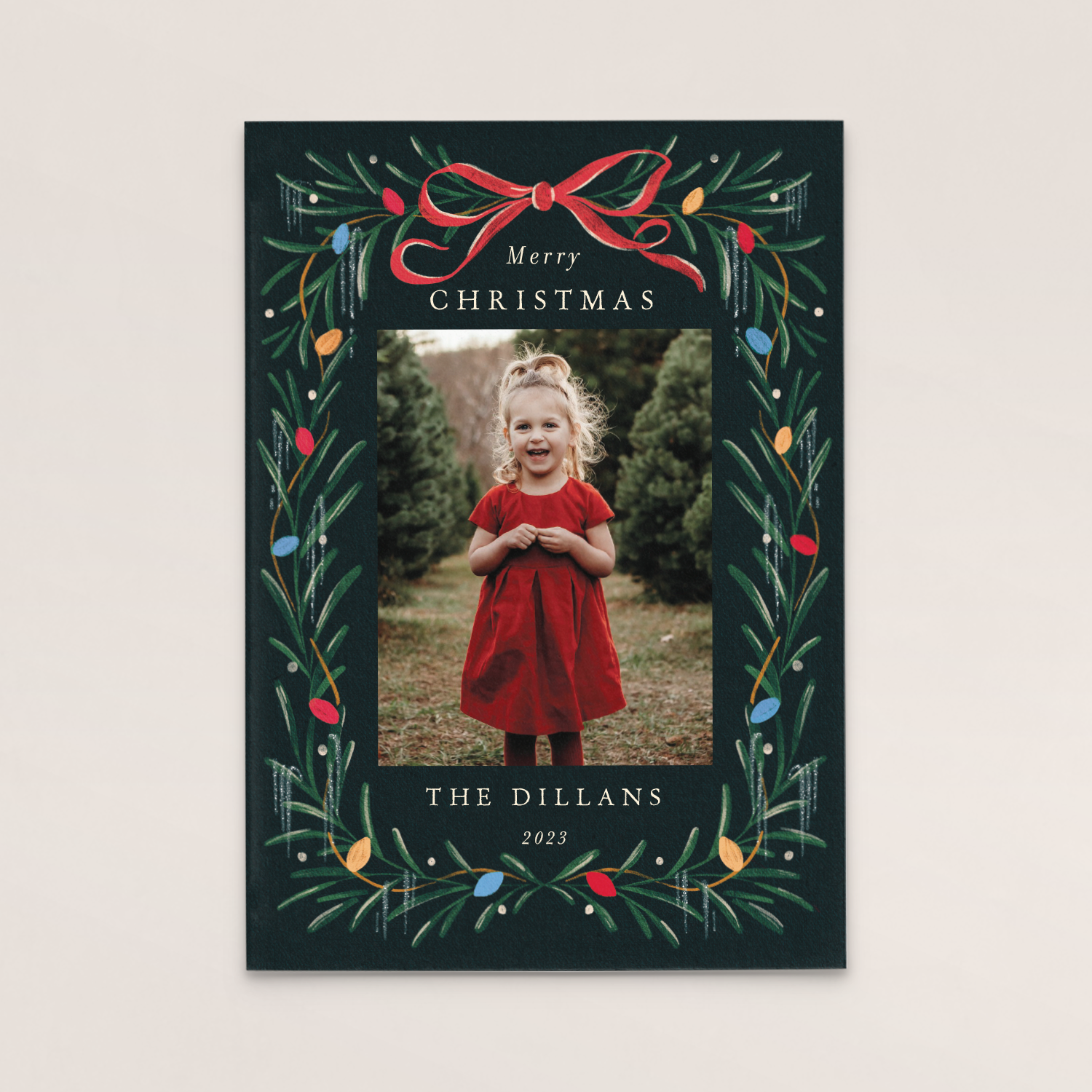 Christmas card with a photo of a young girl in a red dress, standing outdoors among Christmas trees, framed by a festive wreath design with colorful lights and a red bow, and the text 'Merry Christmas,' 'The Dillans,' and '2023.'