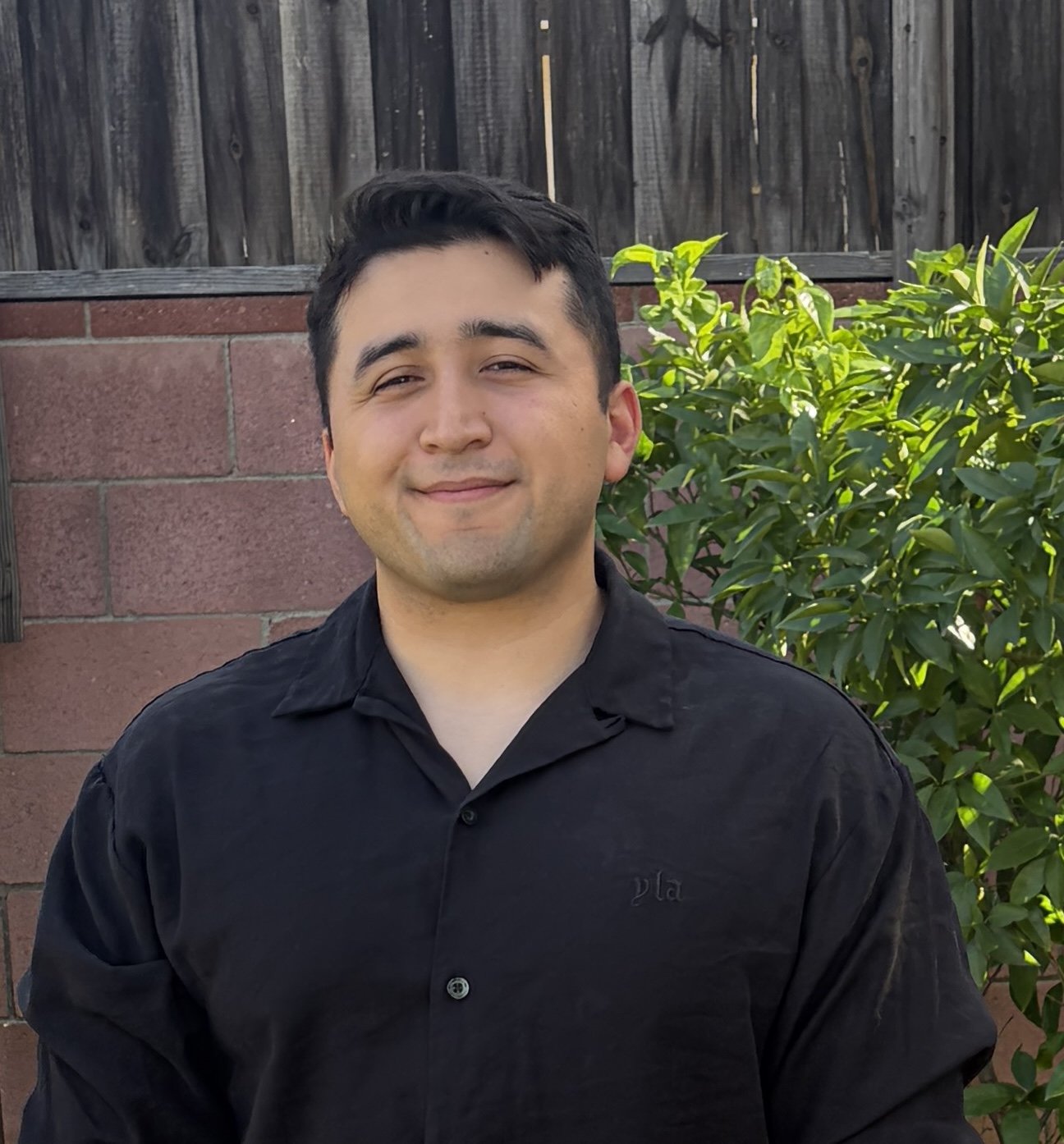 Richard Zamora is an Associate Professional Clinical Counselor with short brown hair standing outdoors in a black shirt, with blurred brick wall in the background.