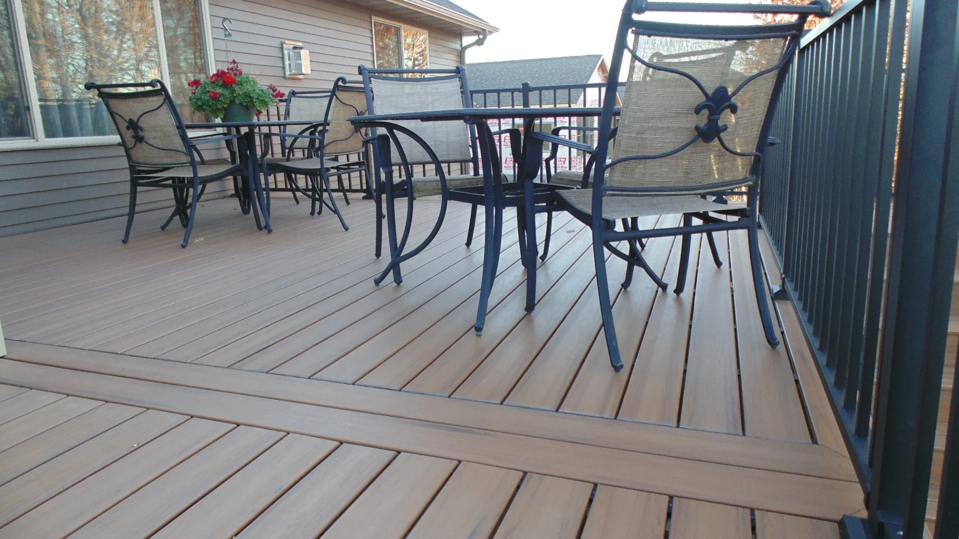 Outdoor deck with metal and concrete patio furniture, including a table and several chairs, with a house wall and windows in the background.