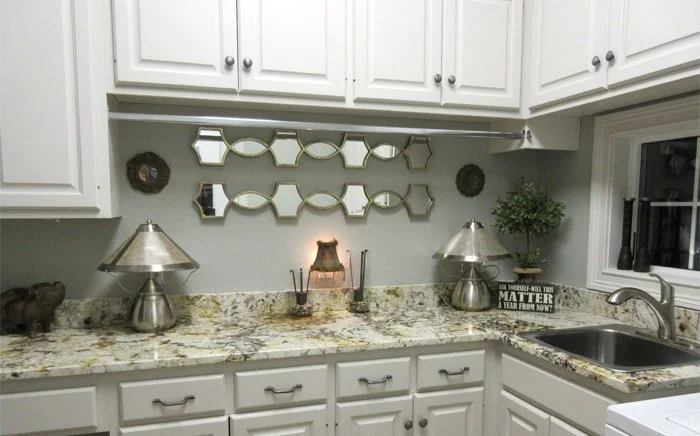 White kitchen countertop with decorative mirrors, two silver lamps, a small potted plant, and a sign that reads 'The Lord is a STRONGHOLD in times of trouble.'